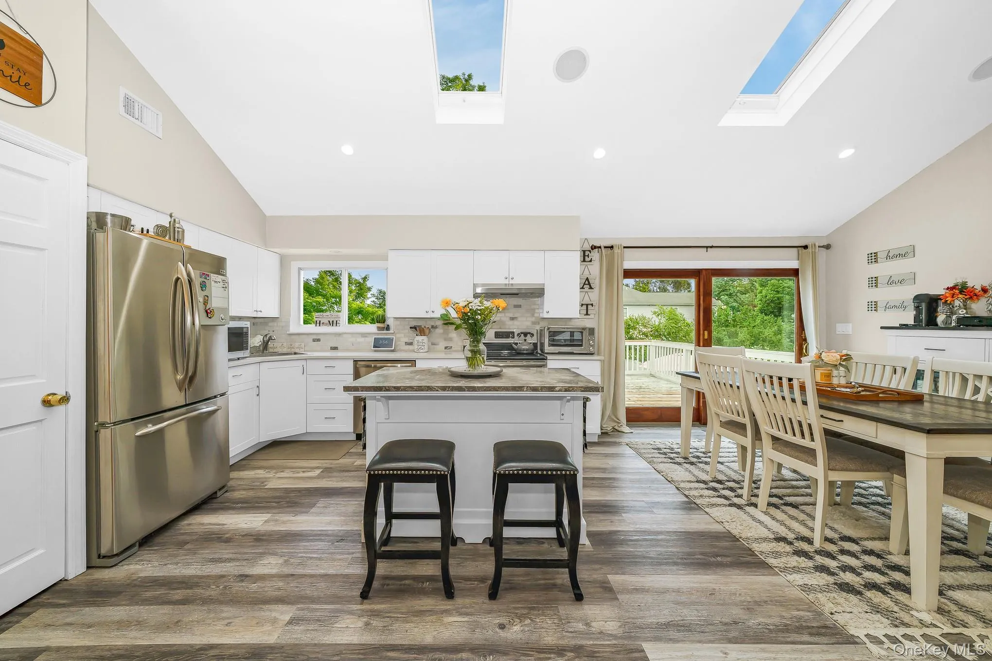 Vaulted ceiling with dual skylights, wood-finish flooring, white cabinetry, stainless steel appliances, and a central island with a contrasting countertop Vaulted ceiling with dual skylights, wood-finish flooring, white cabinetry, stainless steel appliances, and a central island with a contrasting countertop