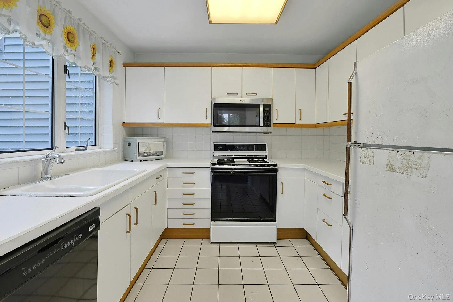U-shaped kitchen with white cabinetry and wood trim, white tile backsplash, and a large window U-shaped kitchen with white cabinetry and wood trim, white tile backsplash, and a large window