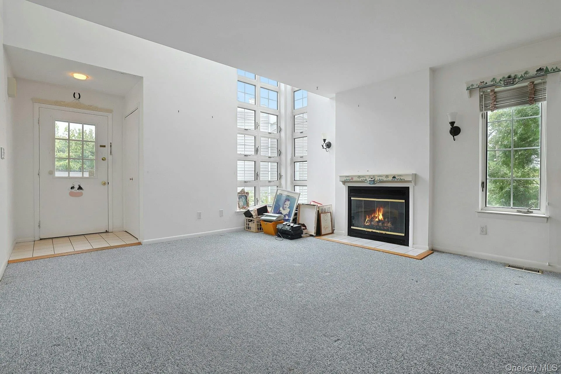 Fireplace with a decorative mantel, large window with natural light, tiled entryway, and vaulted ceiling Fireplace with a decorative mantel, large window with natural light, tiled entryway, and vaulted ceiling