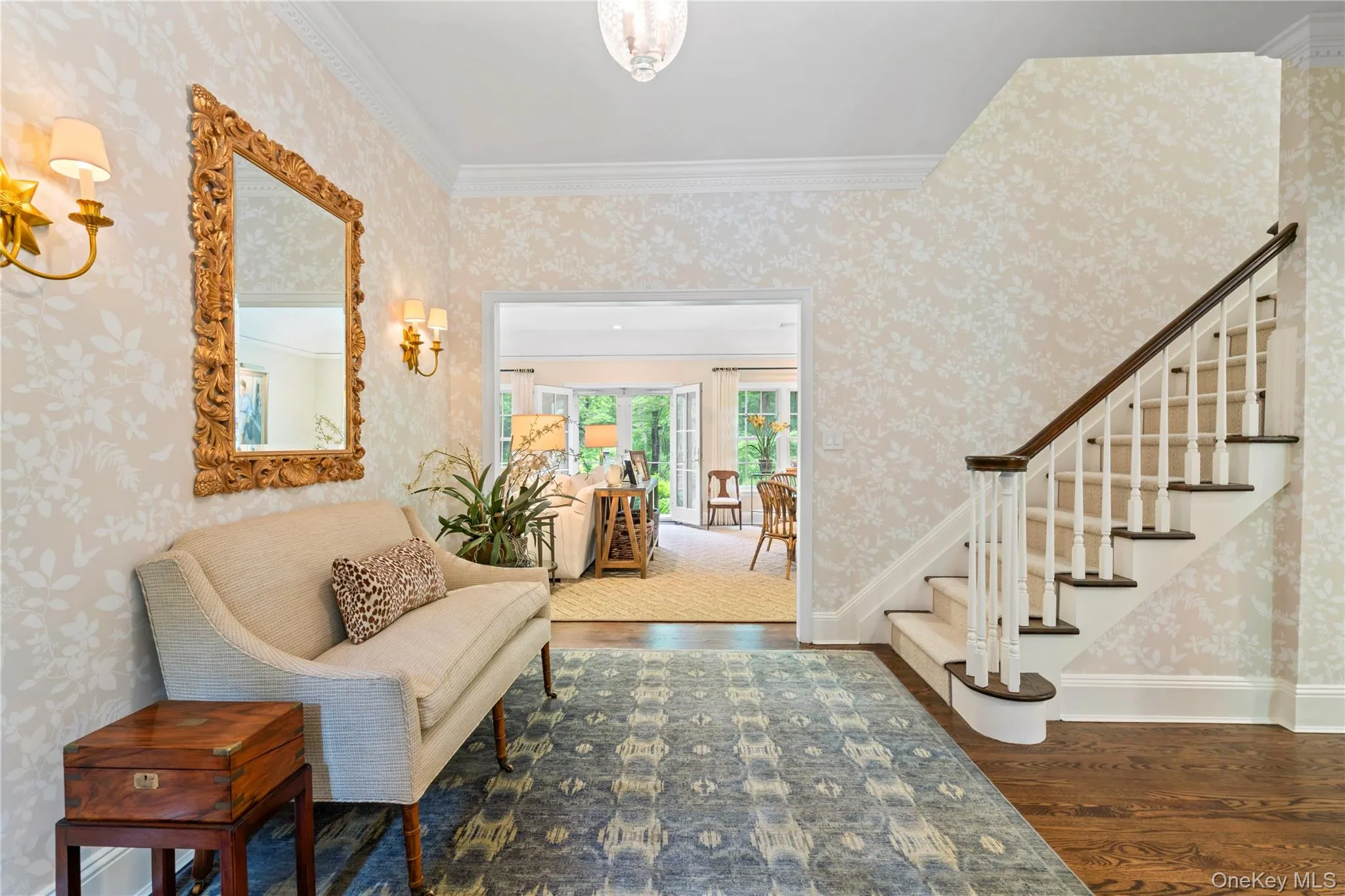 Spacious entrance foyer with wood finished floors, stairs, wallpapered walls, and crown molding Spacious entrance foyer with wood finished floors, stairs, wallpapered walls, and crown molding