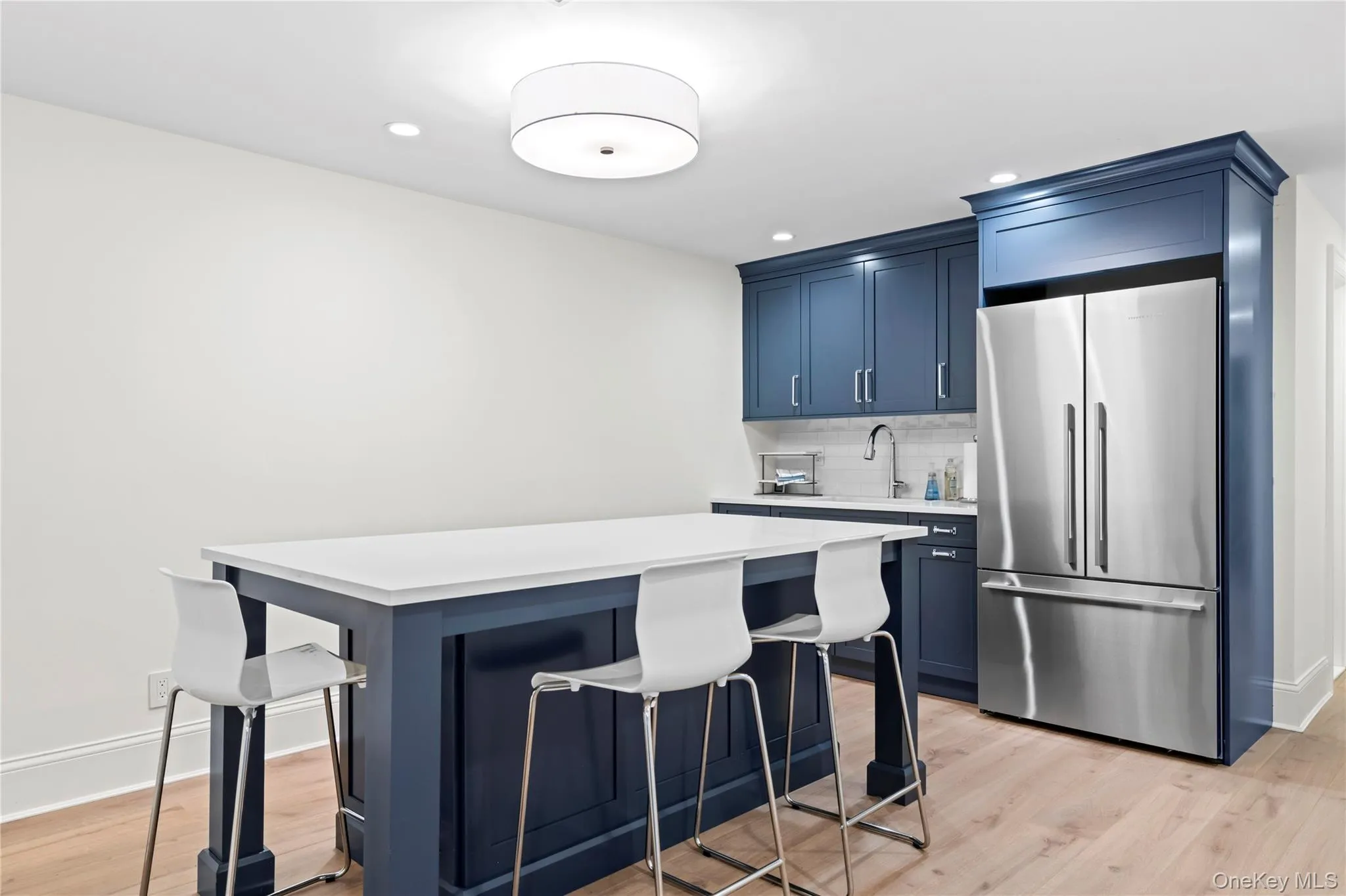 Lower Level Kitchen featuring freestanding Refrigerator, a Kitchen Bar, blue Cabinets, Light Countertops, and Recessed Lighting. Lower Level Kitchen featuring freestanding Refrigerator, a Kitchen Bar, blue Cabinets, Light Countertops, and Recessed Lighting.