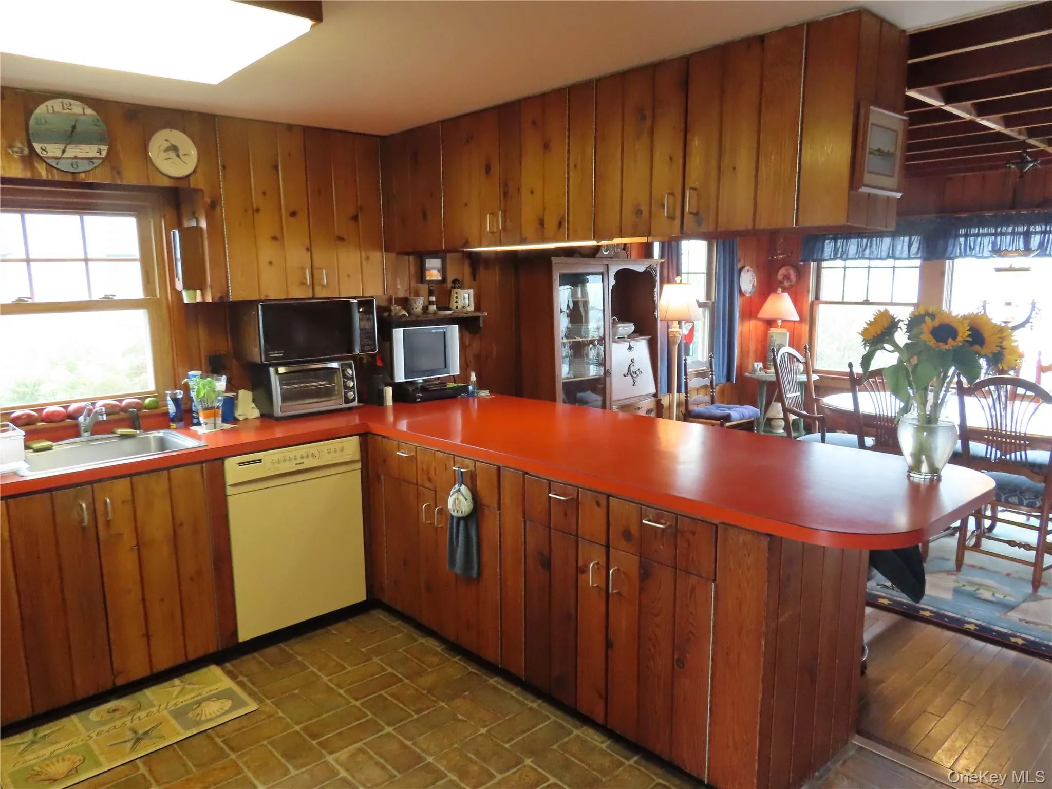 Kitchen with healthy amount of natural light, a peninsula, dishwasher, black microwave, and wood walls Kitchen with healthy amount of natural light, a peninsula, dishwasher, black microwave, and wood walls