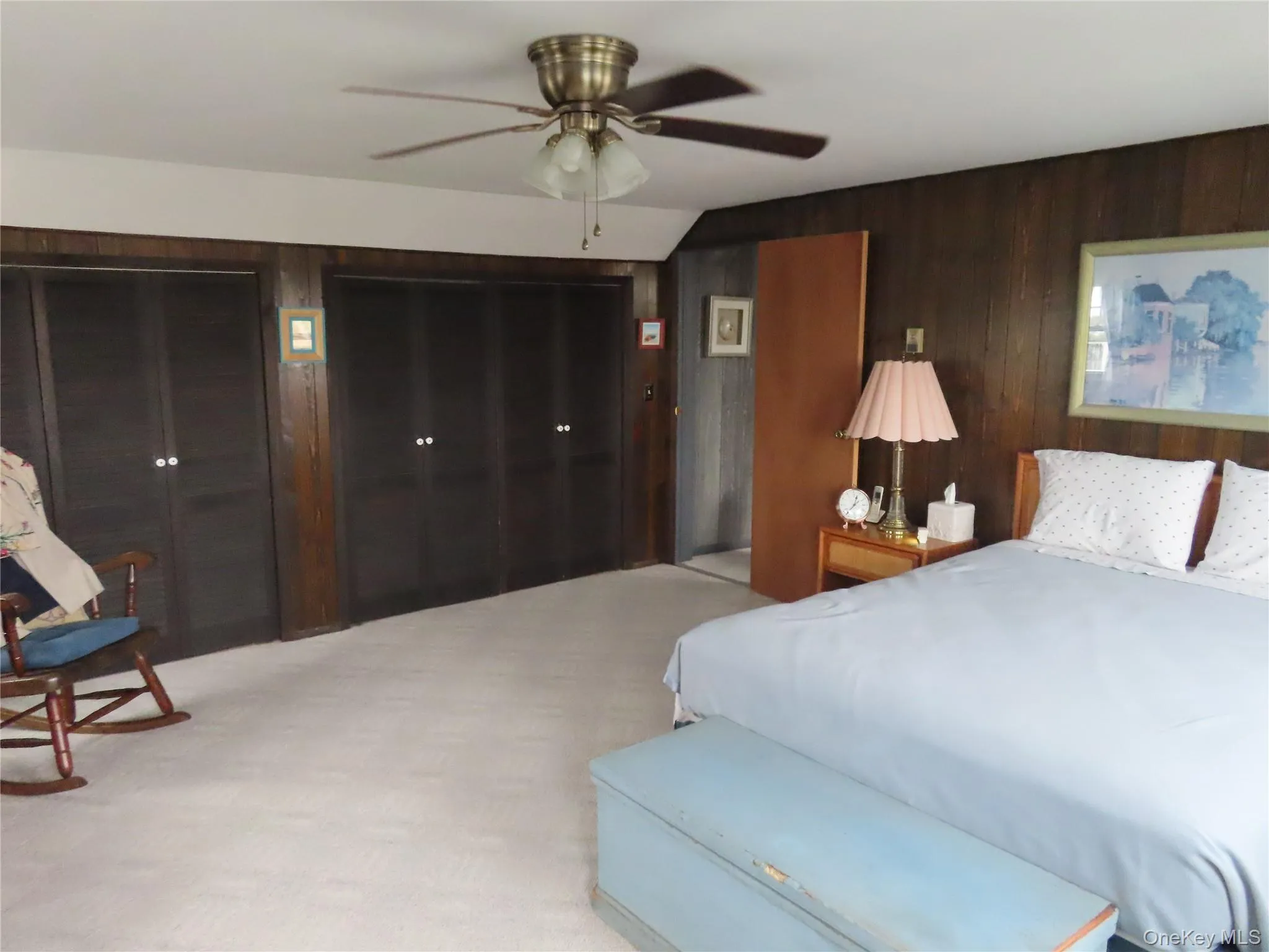 Bedroom featuring wood walls, light colored carpet, two closets, and ceiling fan Bedroom featuring wood walls, light colored carpet, two closets, and ceiling fan