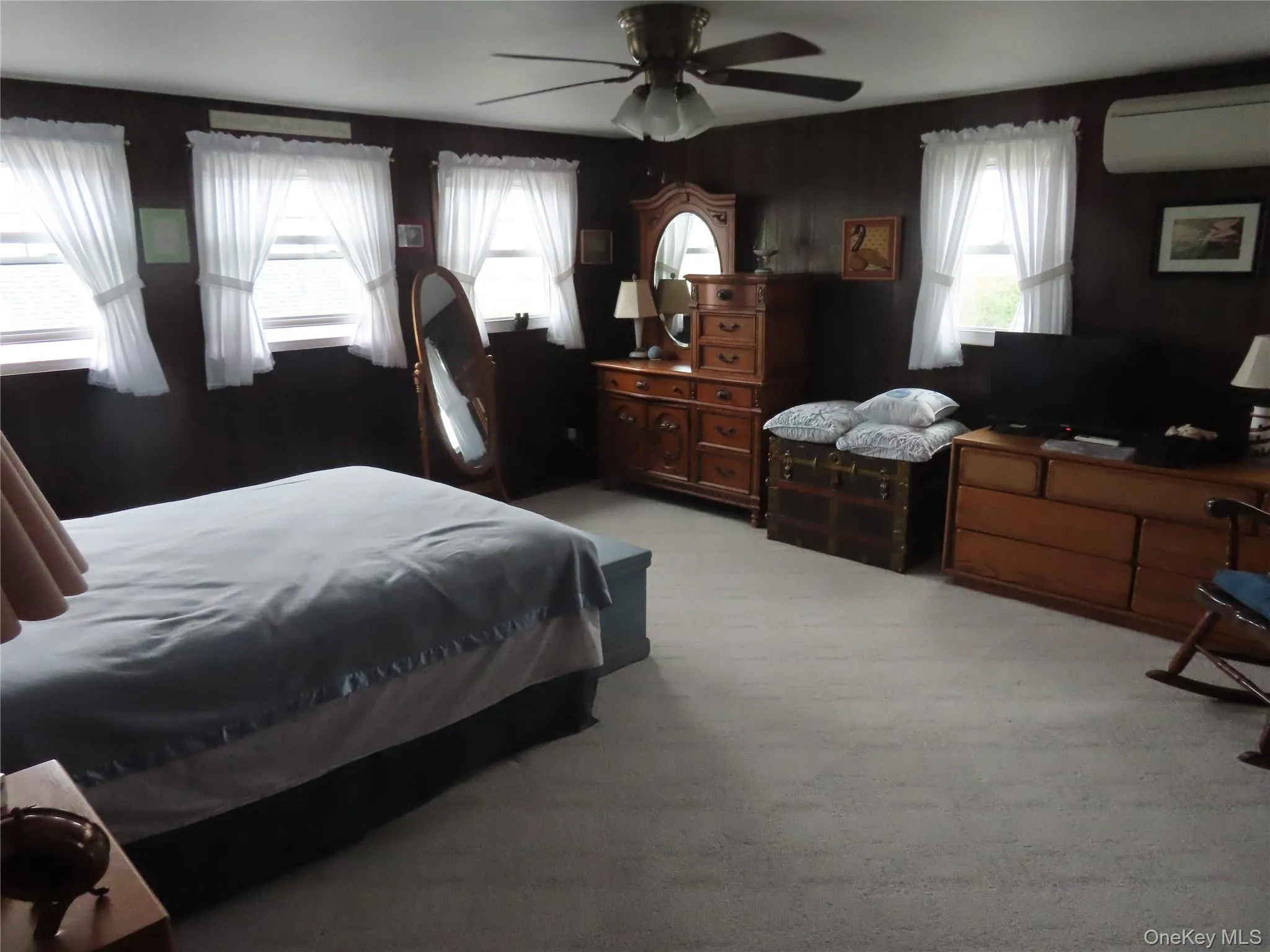 Bedroom featuring a wall unit AC, light colored carpet, ceiling fan, and wooden walls Bedroom featuring a wall unit AC, light colored carpet, ceiling fan, and wooden walls