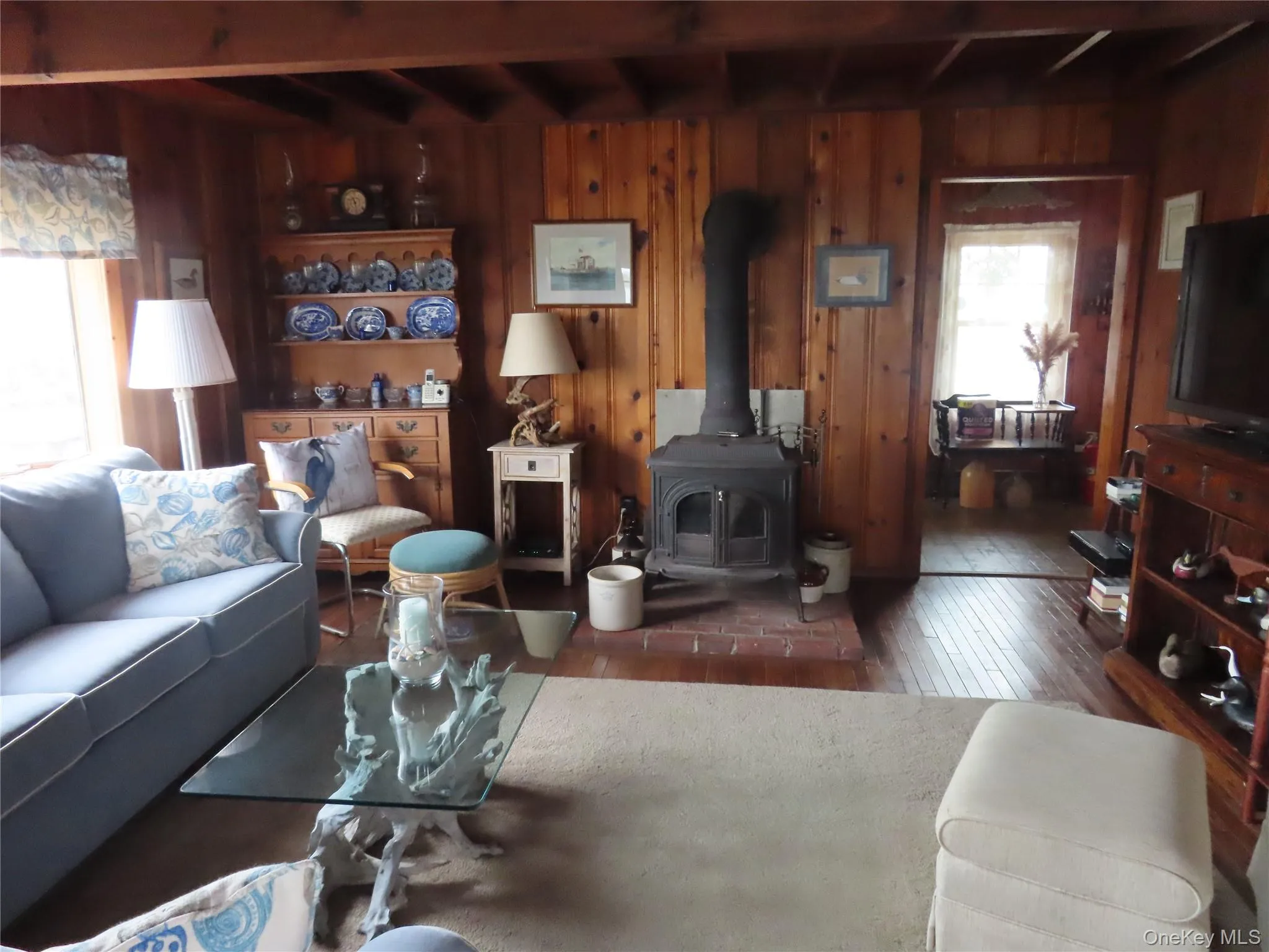 Living area with a wood stove, wood-type flooring, beam ceiling, and wood walls Living area with a wood stove, wood-type flooring, beam ceiling, and wood walls
