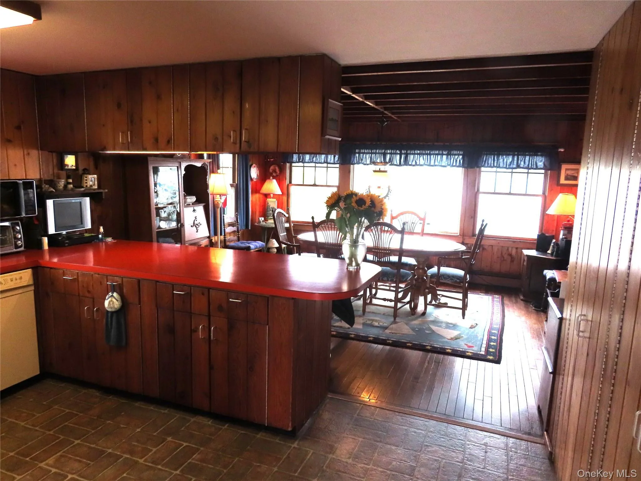 Kitchen featuring wood walls, a peninsula, dark countertops, dishwasher, and dark brown cabinets Kitchen featuring wood walls, a peninsula, dark countertops, dishwasher, and dark brown cabinets
