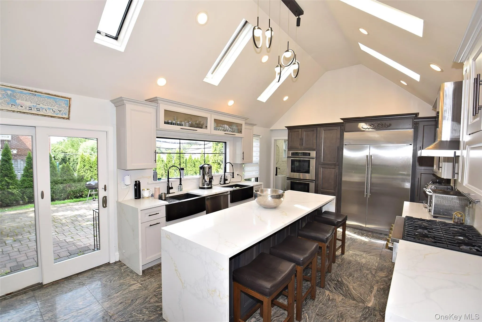 Vaulted ceiling kitchen featuring multiple skylights, recessed lighting, a large island with seating, stainless steel appliances, and a glass-paneled sliding door to the patio Vaulted ceiling kitchen featuring multiple skylights, recessed lighting, a large island with seating, stainless steel appliances, and a glass-paneled sliding door to the patio