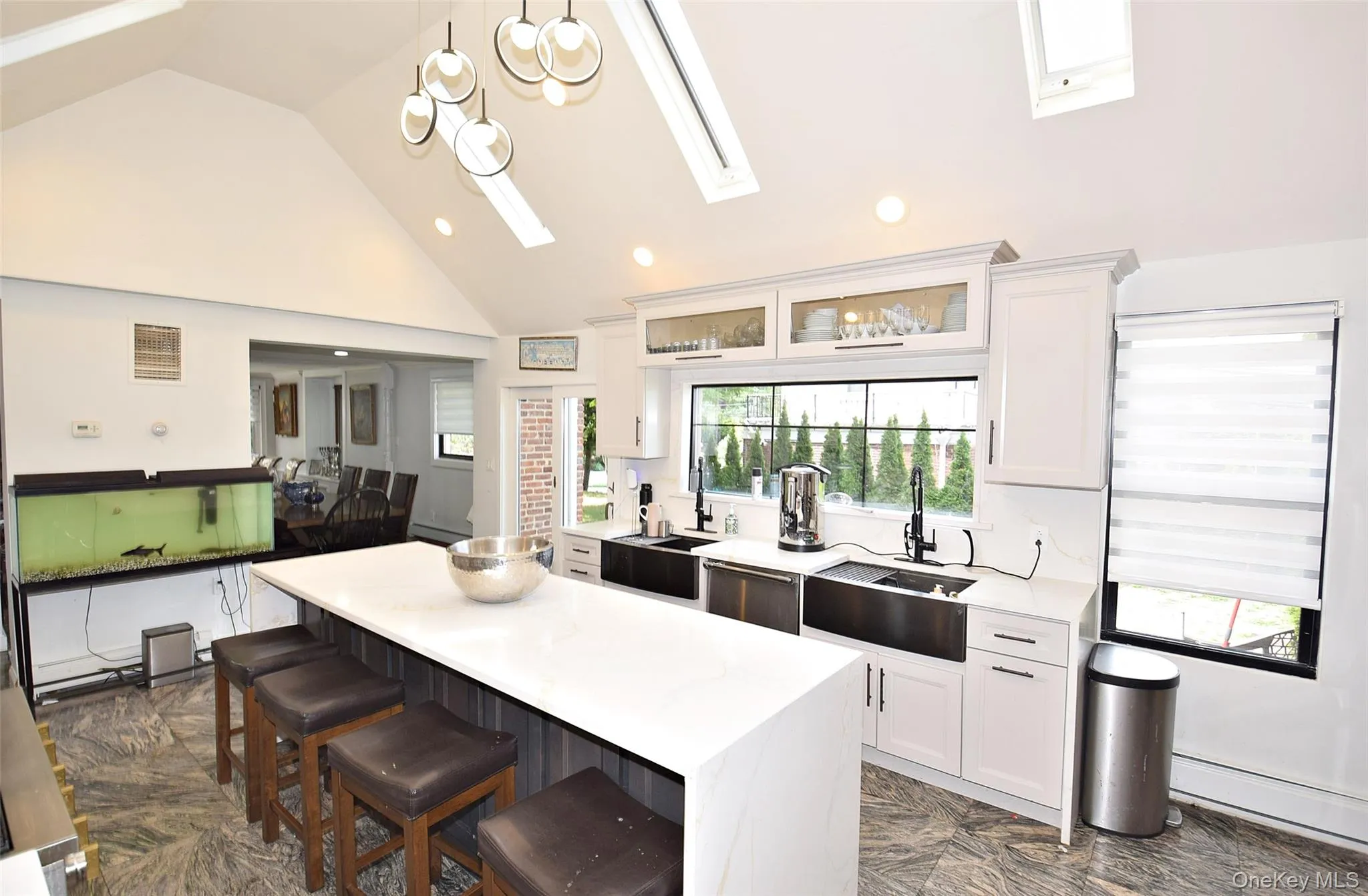 Vaulted ceiling with skylights, contemporary pendant lighting, white shaker cabinetry, dual stainless steel farmhouse sinks, and a large central island with seating Vaulted ceiling with skylights, contemporary pendant lighting, white shaker cabinetry, dual stainless steel farmhouse sinks, and a large central island with seating