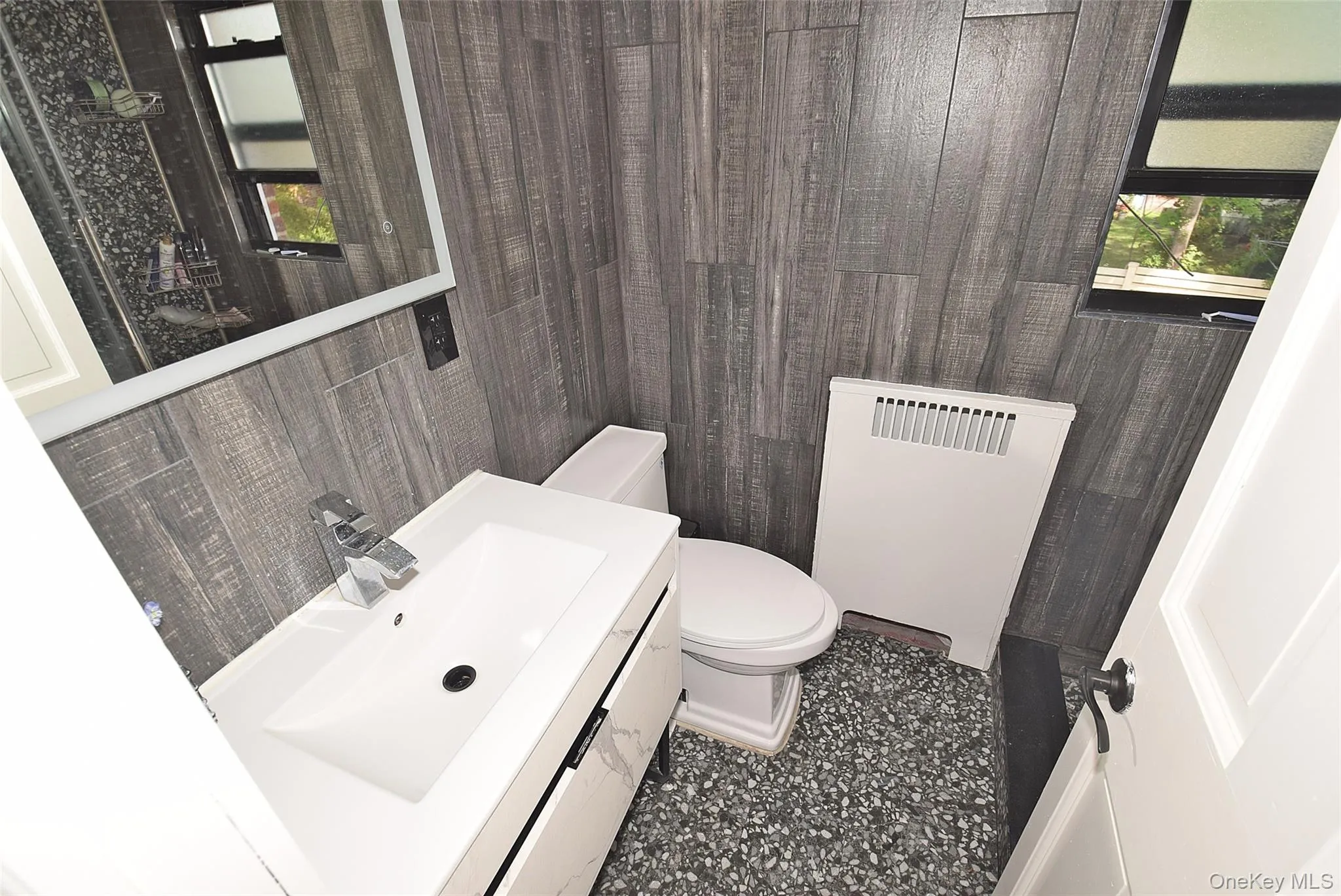 Vanity with an integrated sink, rectangular mirror with backlighting, wood-finish wall paneling. Vanity with an integrated sink, rectangular mirror with backlighting, wood-finish wall paneling.