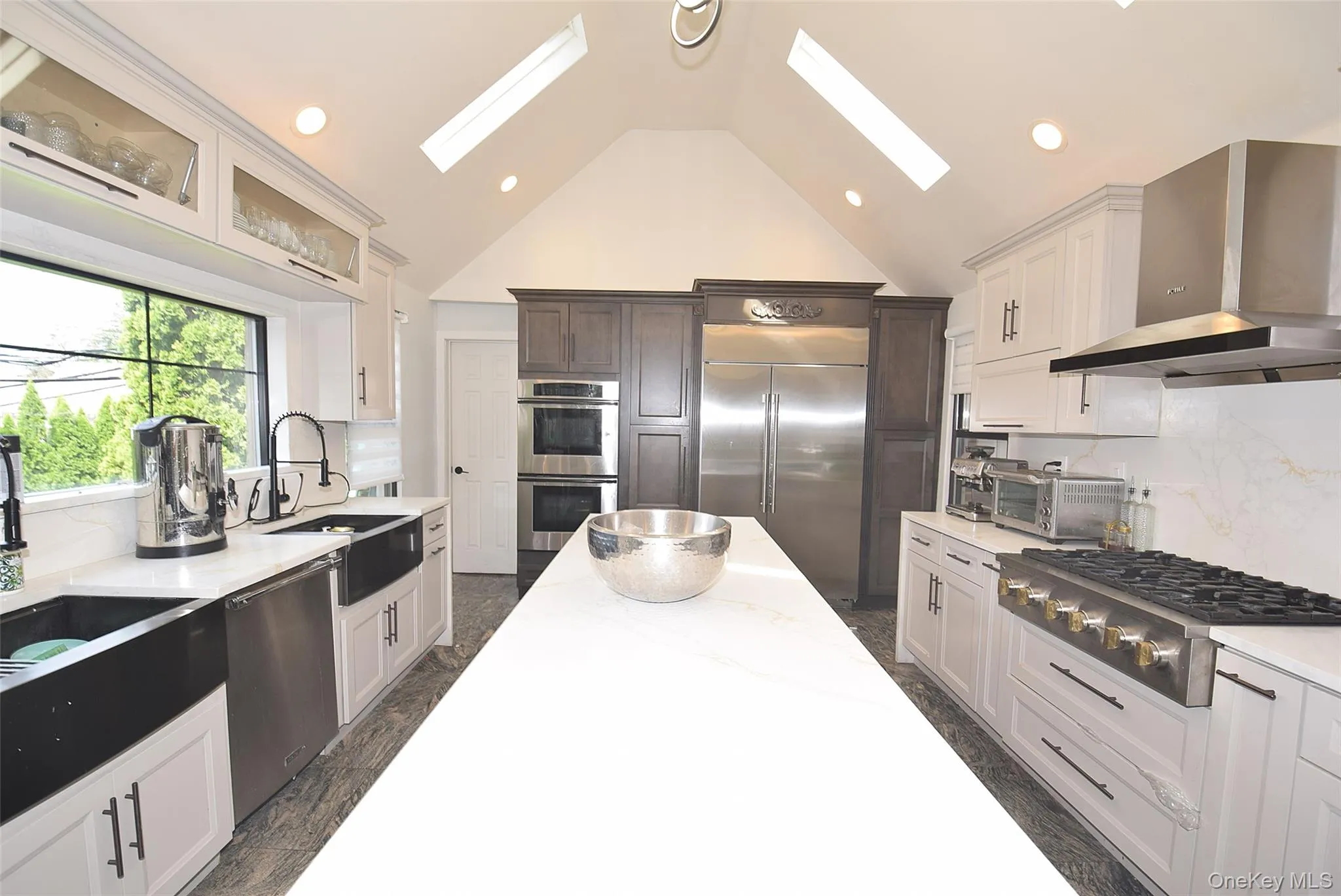 Vaulted ceiling kitchen featuring white cabinetry, a large kitchen island, stainless steel appliances, and skylights Vaulted ceiling kitchen featuring white cabinetry, a large kitchen island, stainless steel appliances, and skylights