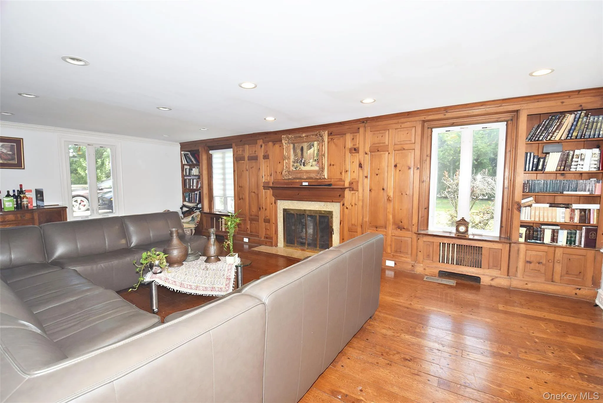 Wood-paneled accent wall, built-in shelving, wood-finish flooring, recessed lighting, and a stone-surround fireplace Wood-paneled accent wall, built-in shelving, wood-finish flooring, recessed lighting, and a stone-surround fireplace
