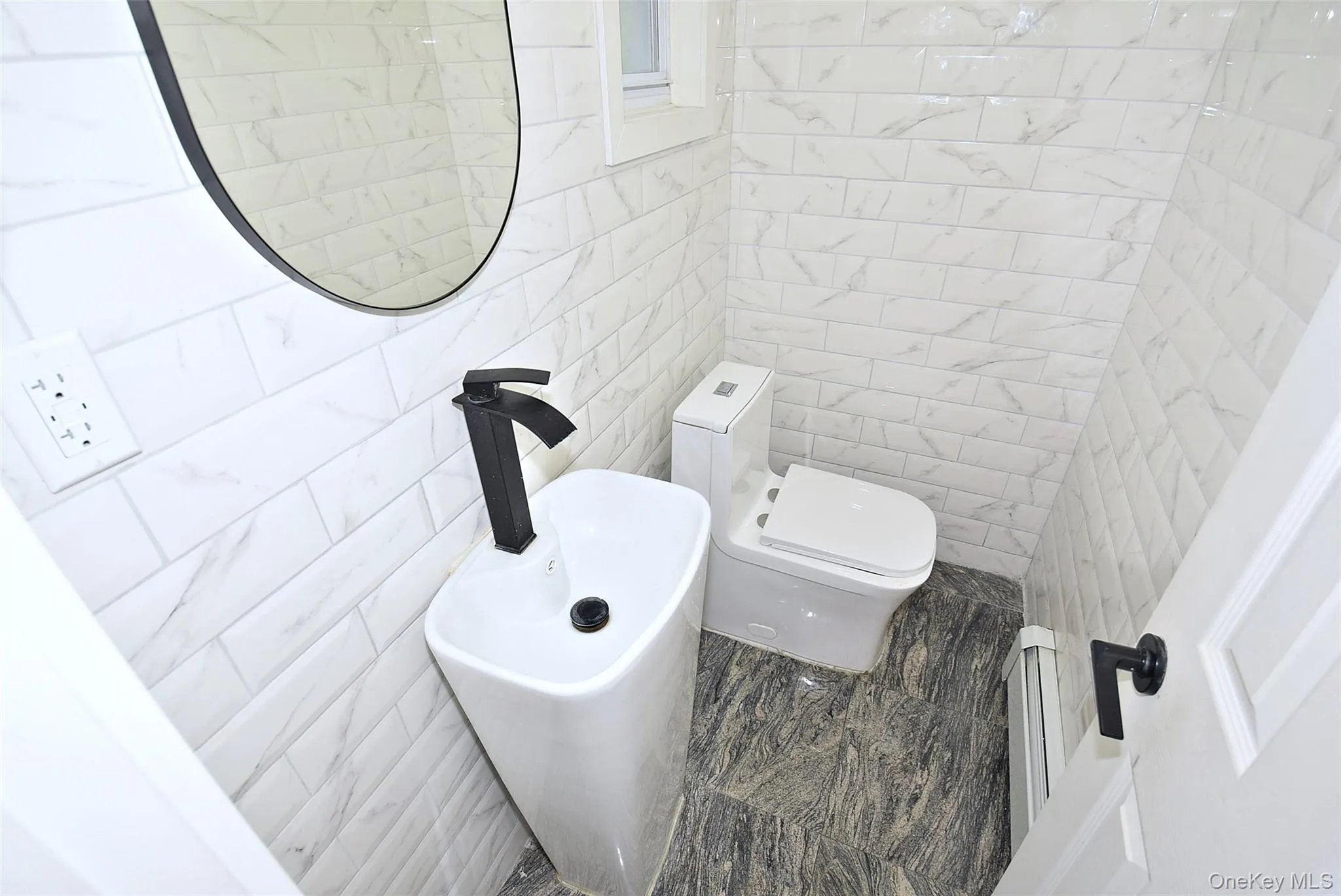 Half bath with window. White subway tile walls with subtle veining, modern pedestal sink with matte black faucet, and a contemporary toilet Half bath with window. White subway tile walls with subtle veining, modern pedestal sink with matte black faucet, and a contemporary toilet