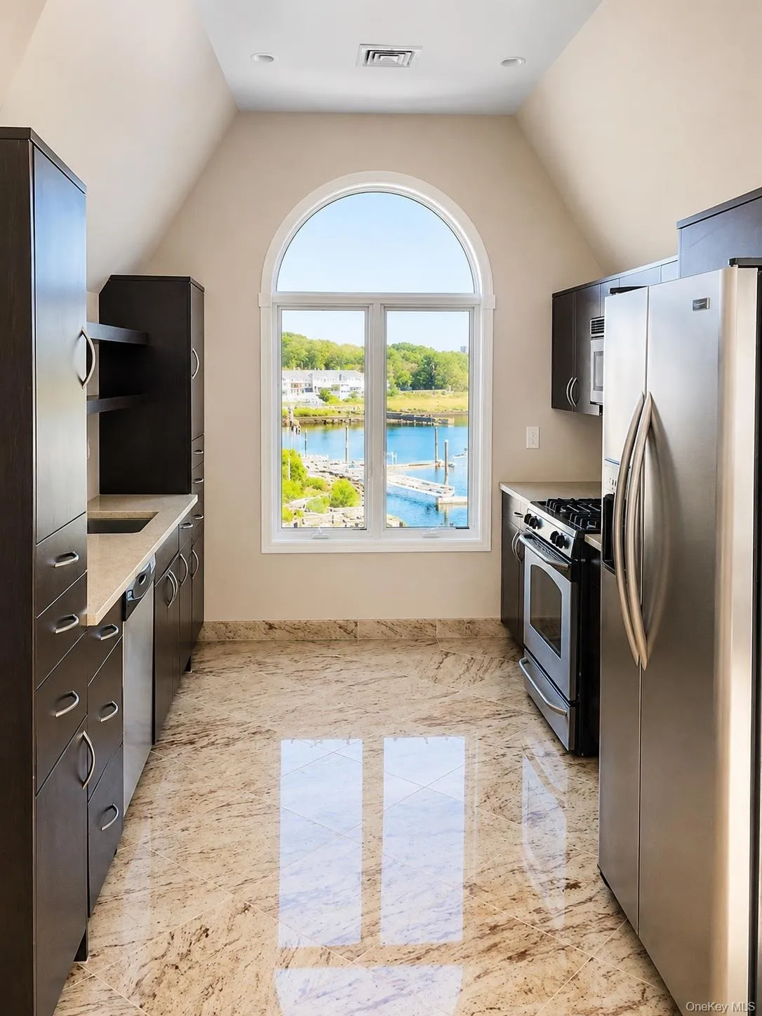 Arched window with water scenery, dark wood-finish cabinetry, stainless steel appliances, light-toned countertop, and polished tile flooring Arched window with water scenery, dark wood-finish cabinetry, stainless steel appliances, light-toned countertop, and polished tile flooring