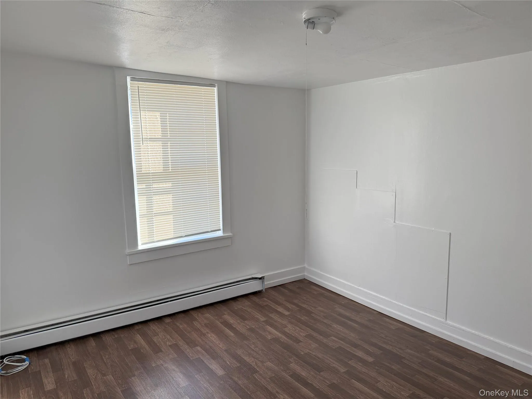 Empty room with dark wood-type flooring and a baseboard radiator Empty room with dark wood-type flooring and a baseboard radiator