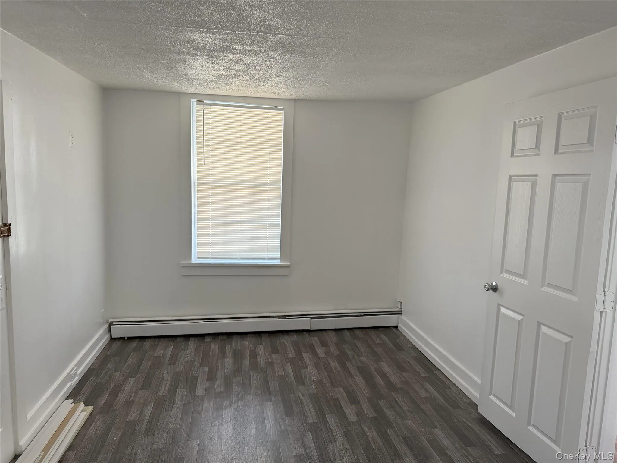Spare room with a baseboard heating unit, dark wood-type flooring, and a textured ceiling Spare room with a baseboard heating unit, dark wood-type flooring, and a textured ceiling