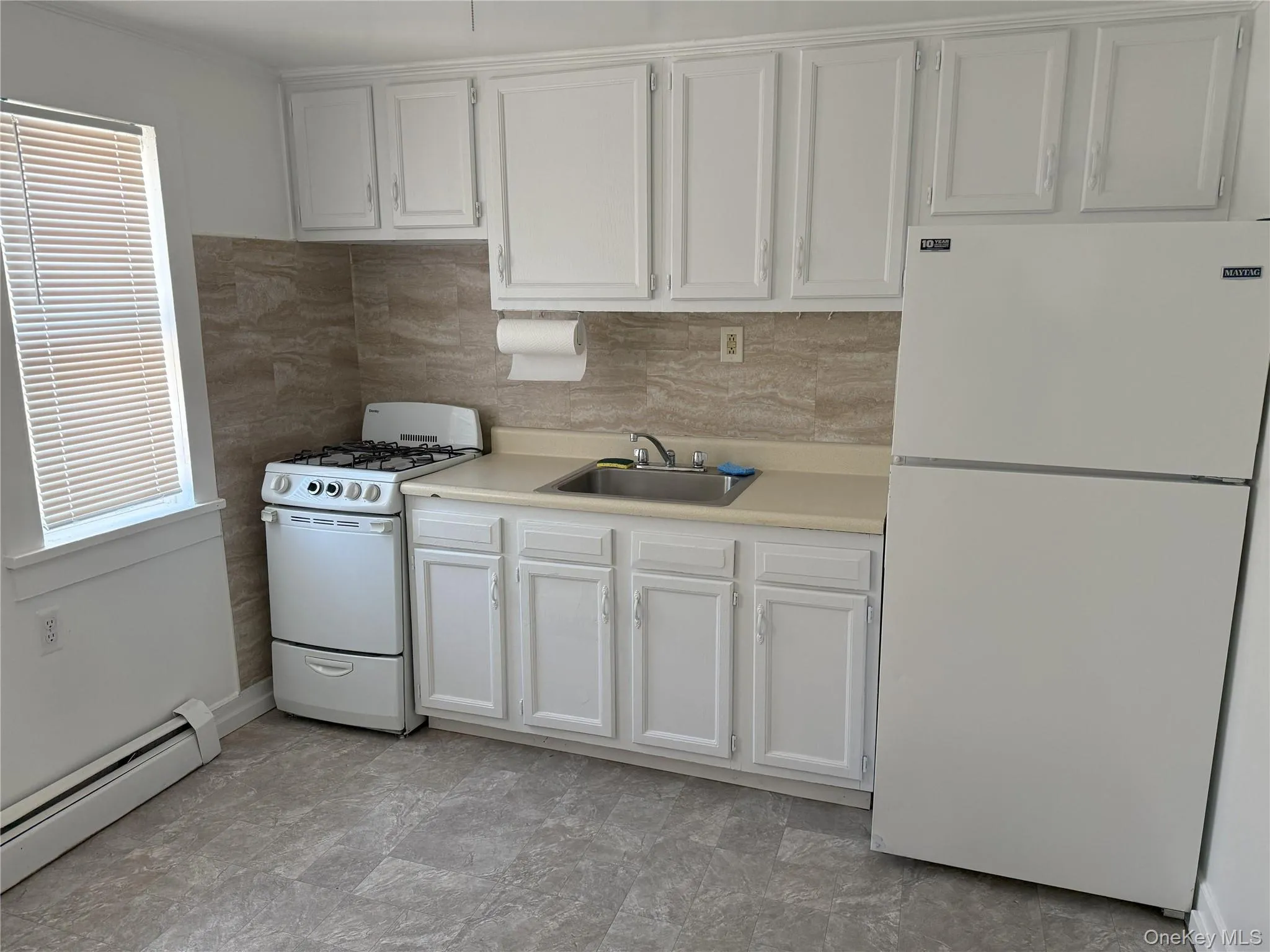 Kitchen featuring sink, white appliances, white cabinetry, tasteful backsplash, and a baseboard radiator Kitchen featuring sink, white appliances, white cabinetry, tasteful backsplash, and a baseboard radiator