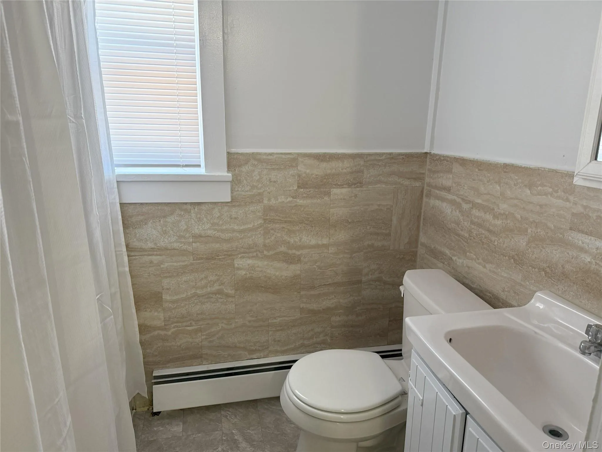 Bathroom with vanity, toilet, tile walls, and a baseboard heating unit Bathroom with vanity, toilet, tile walls, and a baseboard heating unit