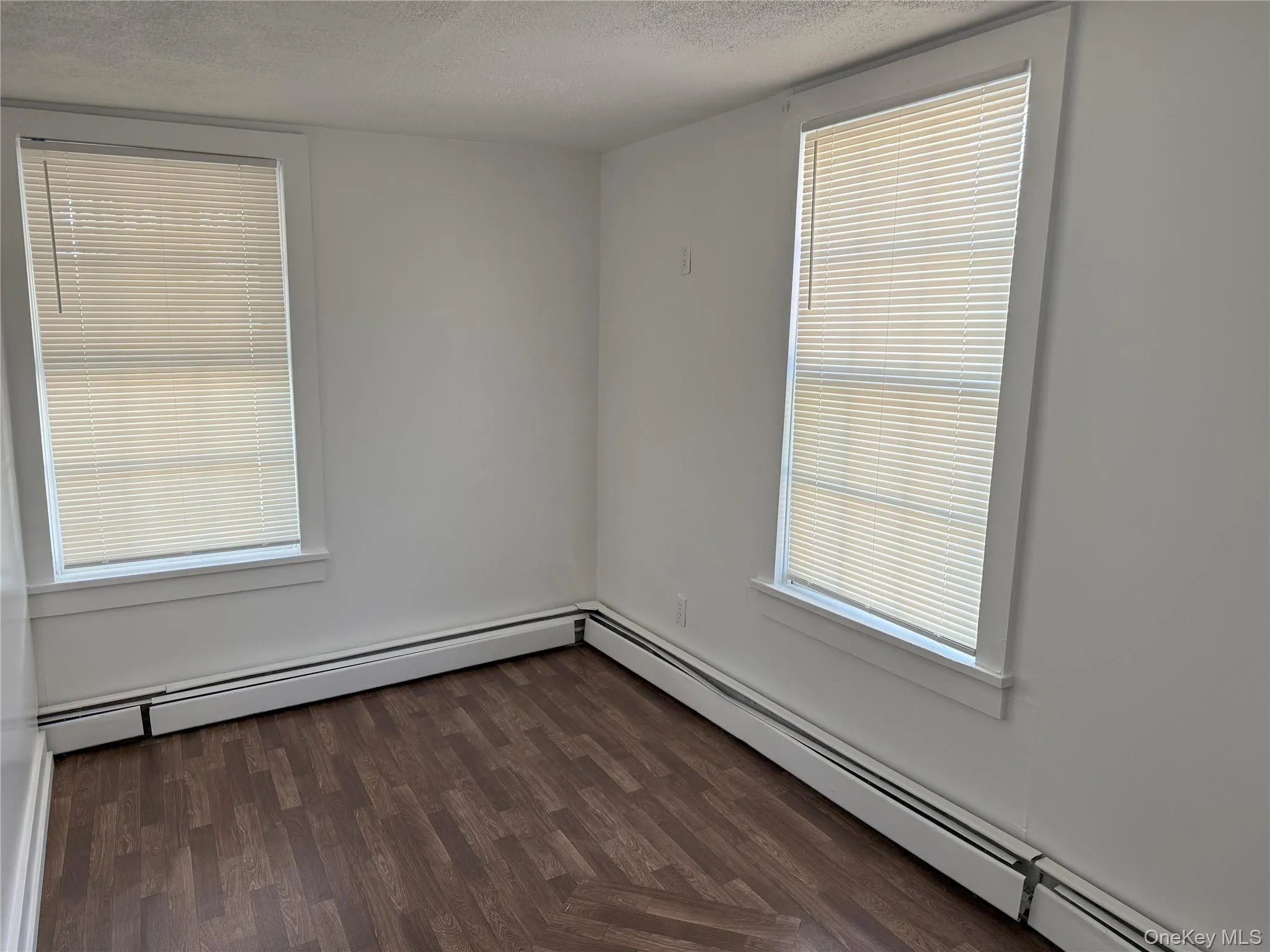 Unfurnished room with a baseboard heating unit, dark wood-type flooring, and a textured ceiling Unfurnished room with a baseboard heating unit, dark wood-type flooring, and a textured ceiling