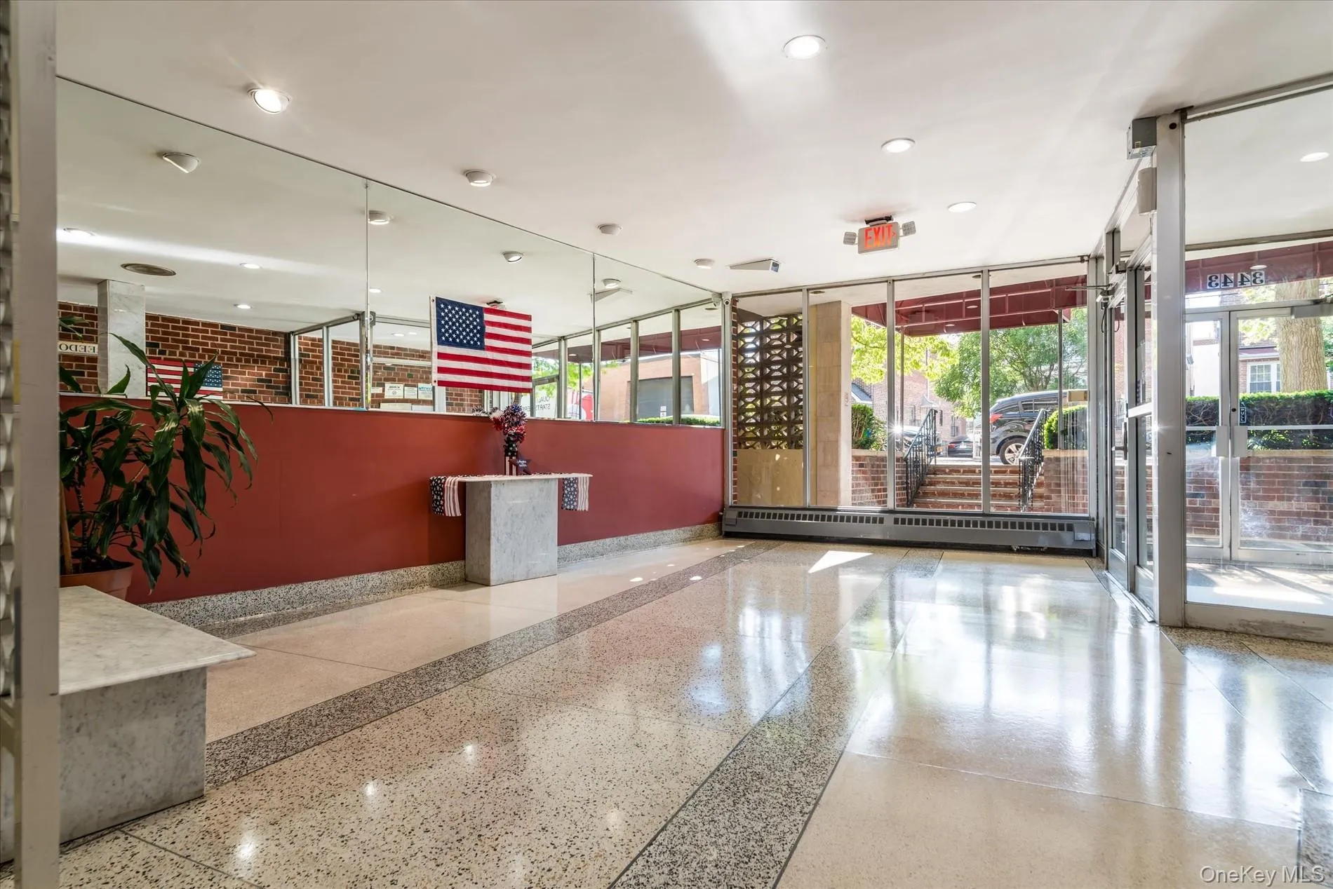 Polished terrazzo flooring, expansive full-height windows, a mirrored wall, recessed lighting, and a red brick wall Polished terrazzo flooring, expansive full-height windows, a mirrored wall, recessed lighting, and a red brick wall