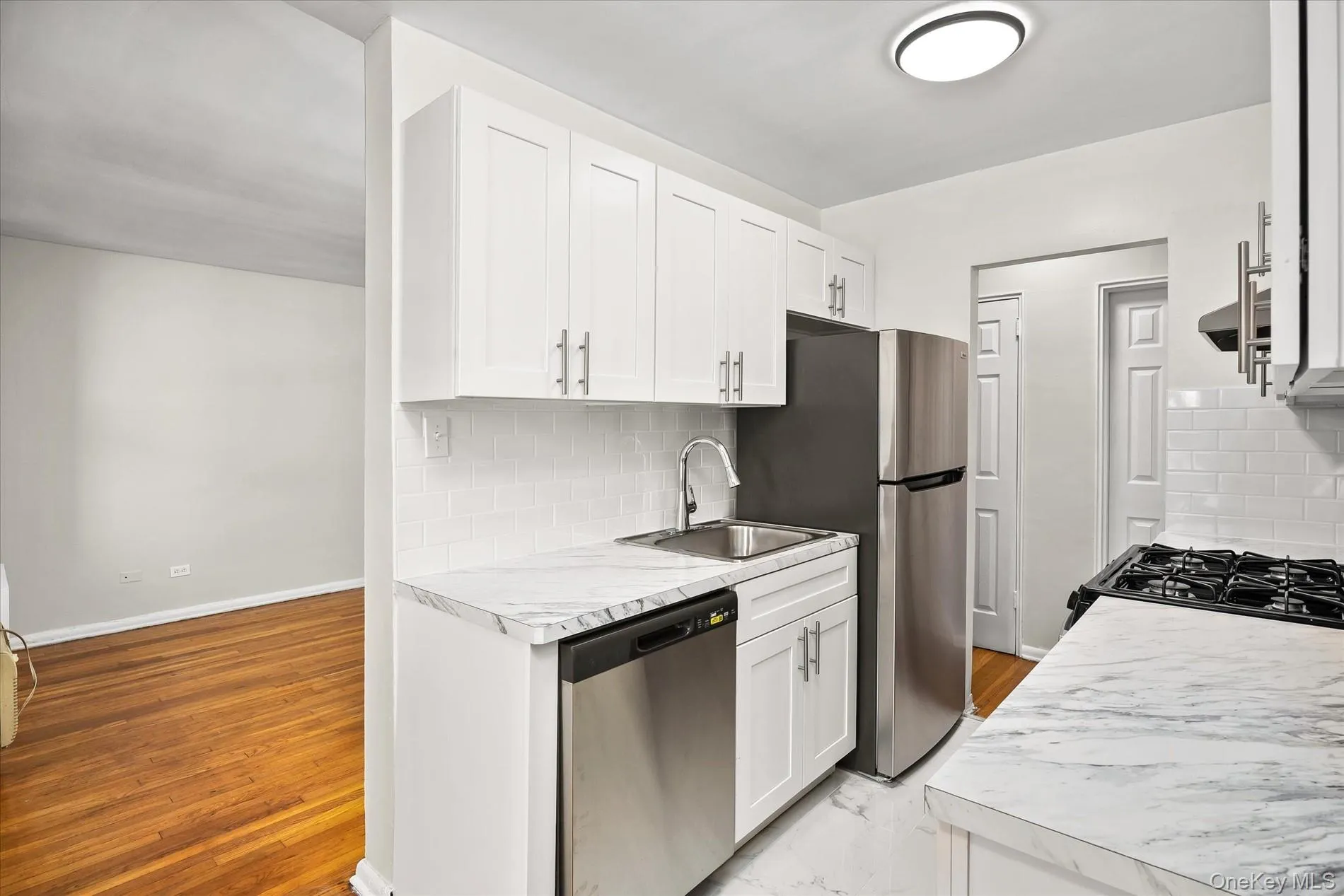 Kitchen featuring white shaker cabinetry, stainless steel appliances, marble-look countertops, subway tile backsplash, and a gas range Kitchen featuring white shaker cabinetry, stainless steel appliances, marble-look countertops, subway tile backsplash, and a gas range
