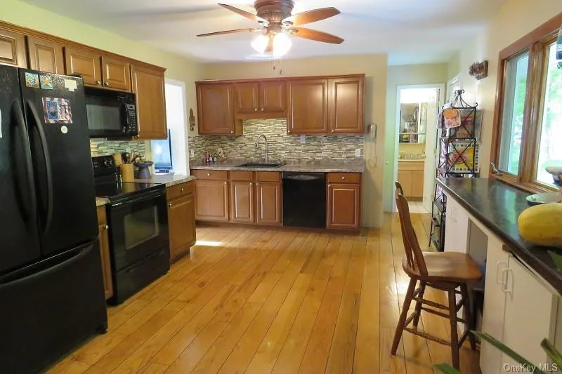 Hardwood flooring, wood cabinetry, stone-look countertops, tile backsplash, and a ceiling fan Hardwood flooring, wood cabinetry, stone-look countertops, tile backsplash, and a ceiling fan