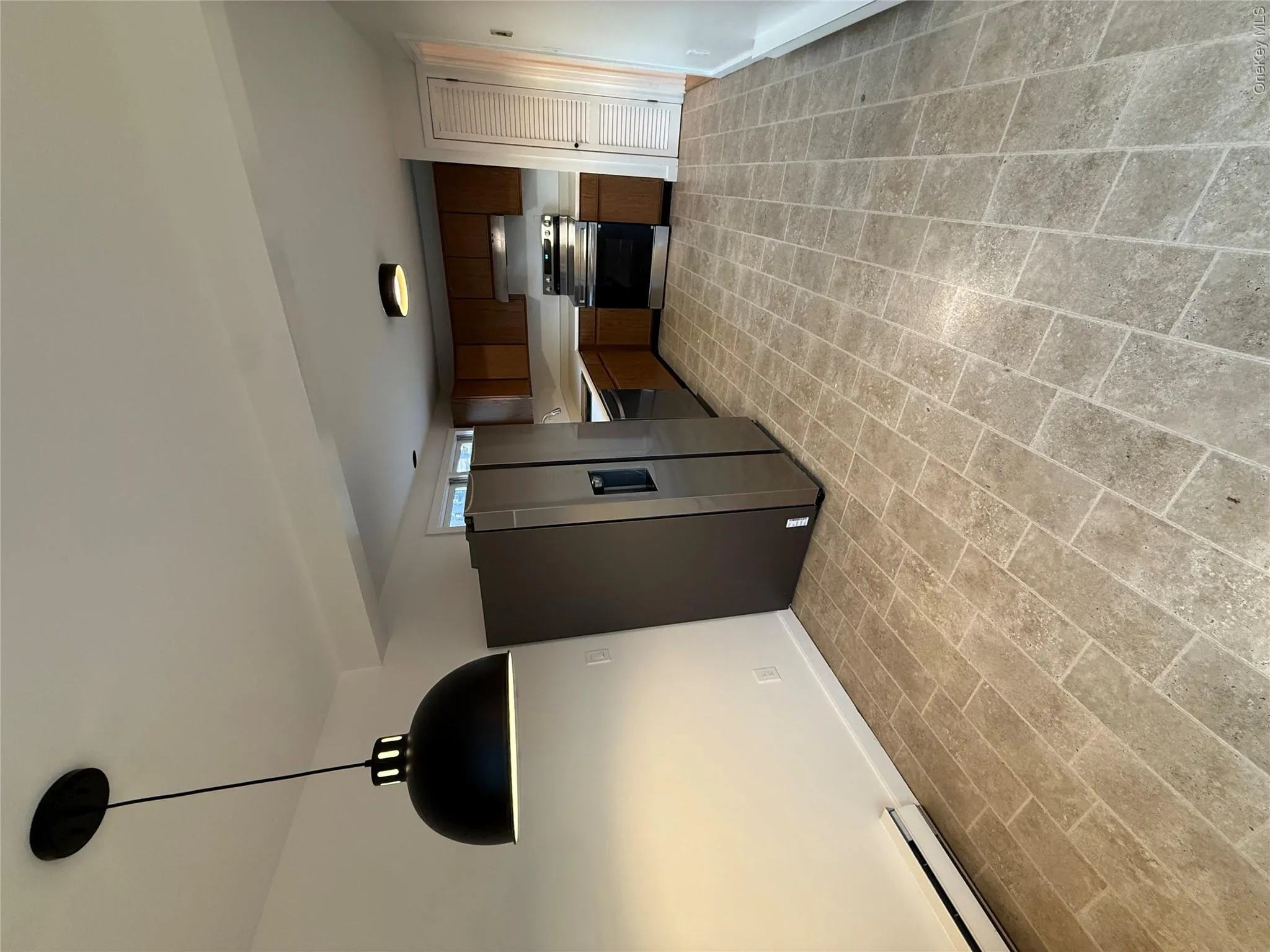 Kitchen with appliances with stainless steel finishes, baseboard heating, light countertops, brick patterned floors, and decorative light fixtures Kitchen with appliances with stainless steel finishes, baseboard heating, light countertops, brick patterned floors, and decorative light fixtures
