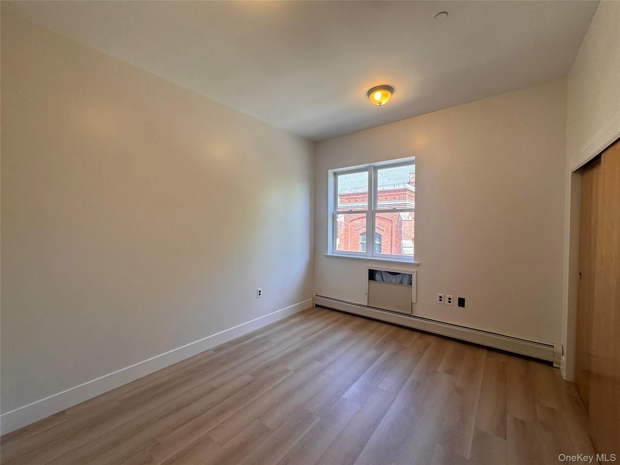 Wood-finish flooring, neutral wall tones, window with natural light, integrated wall heating unit, and built-in closet with wood-finish sliding doors Wood-finish flooring, neutral wall tones, window with natural light, integrated wall heating unit, and built-in closet with wood-finish sliding doors