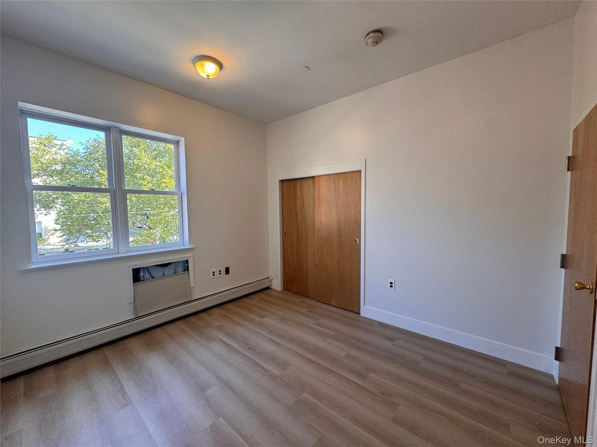 Wood-finish flooring, built-in closet with natural wood doors, white trim, and a window with white casing Wood-finish flooring, built-in closet with natural wood doors, white trim, and a window with white casing