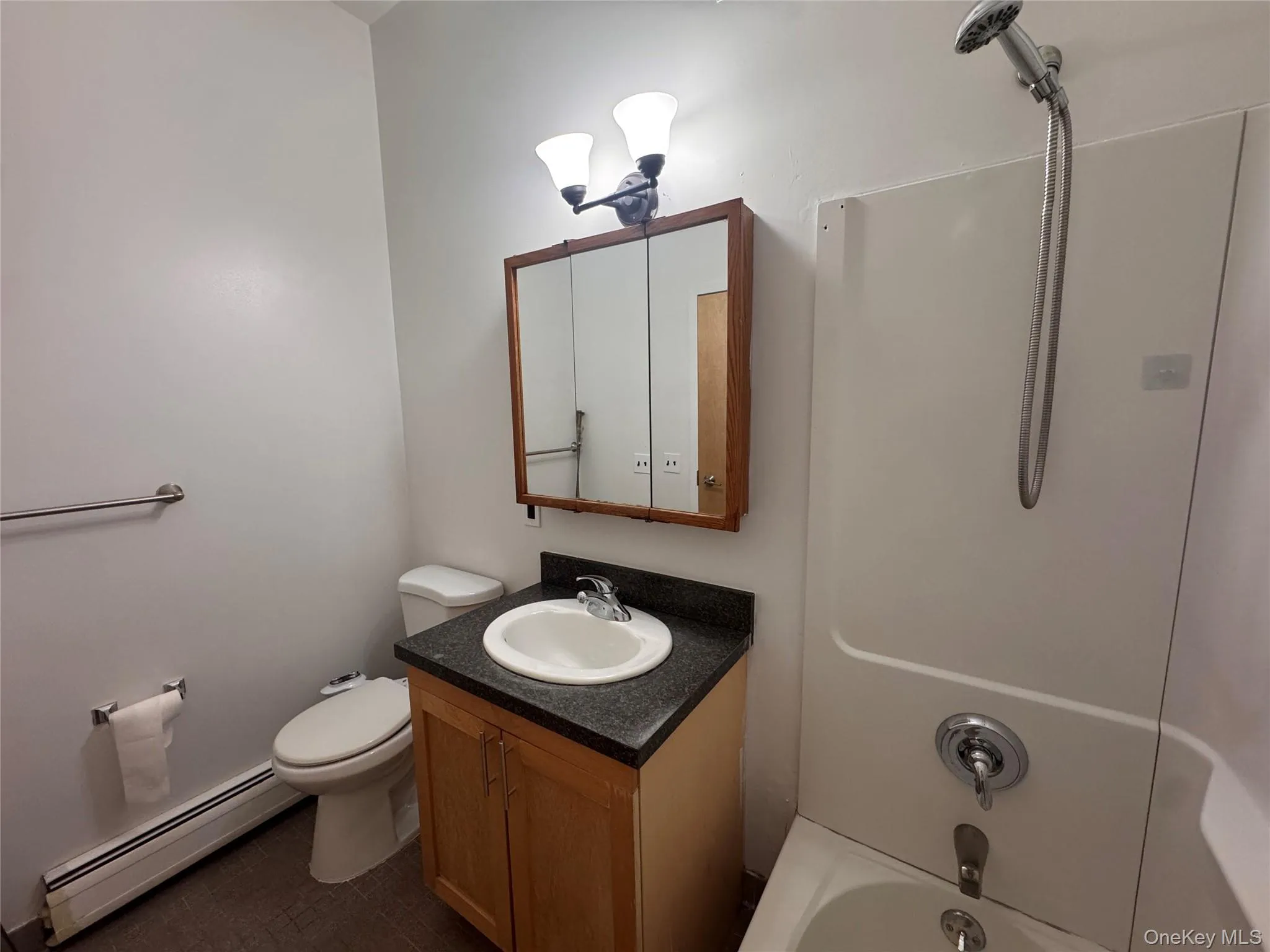 Bathroom featuring a tub/shower combination, a vanity with a white basin and dark countertop, and a medicine cabinet with a wood-finish frame Bathroom featuring a tub/shower combination, a vanity with a white basin and dark countertop, and a medicine cabinet with a wood-finish frame