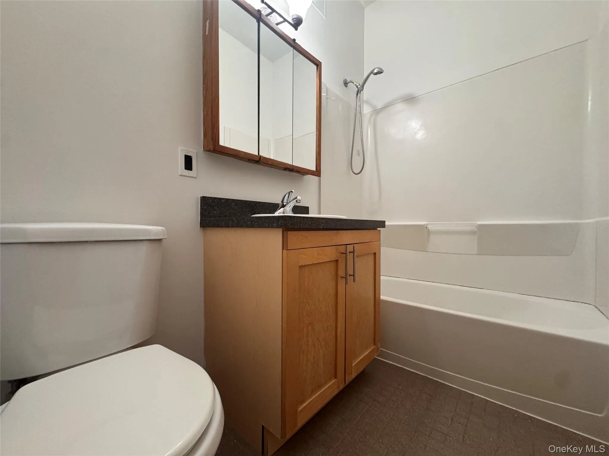 Bathroom featuring a single vanity with wood-finish cabinetry, dark countertop, and integrated sink Bathroom featuring a single vanity with wood-finish cabinetry, dark countertop, and integrated sink