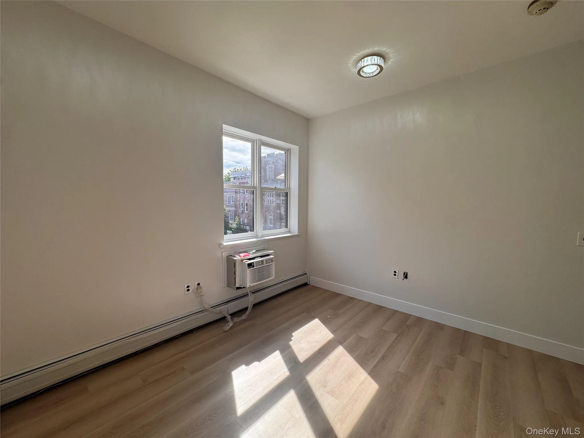 Recessed ceiling light fixture, wood-finish flooring, white trim, window-mounted air conditioning unit, and baseboard heating Recessed ceiling light fixture, wood-finish flooring, white trim, window-mounted air conditioning unit, and baseboard heating