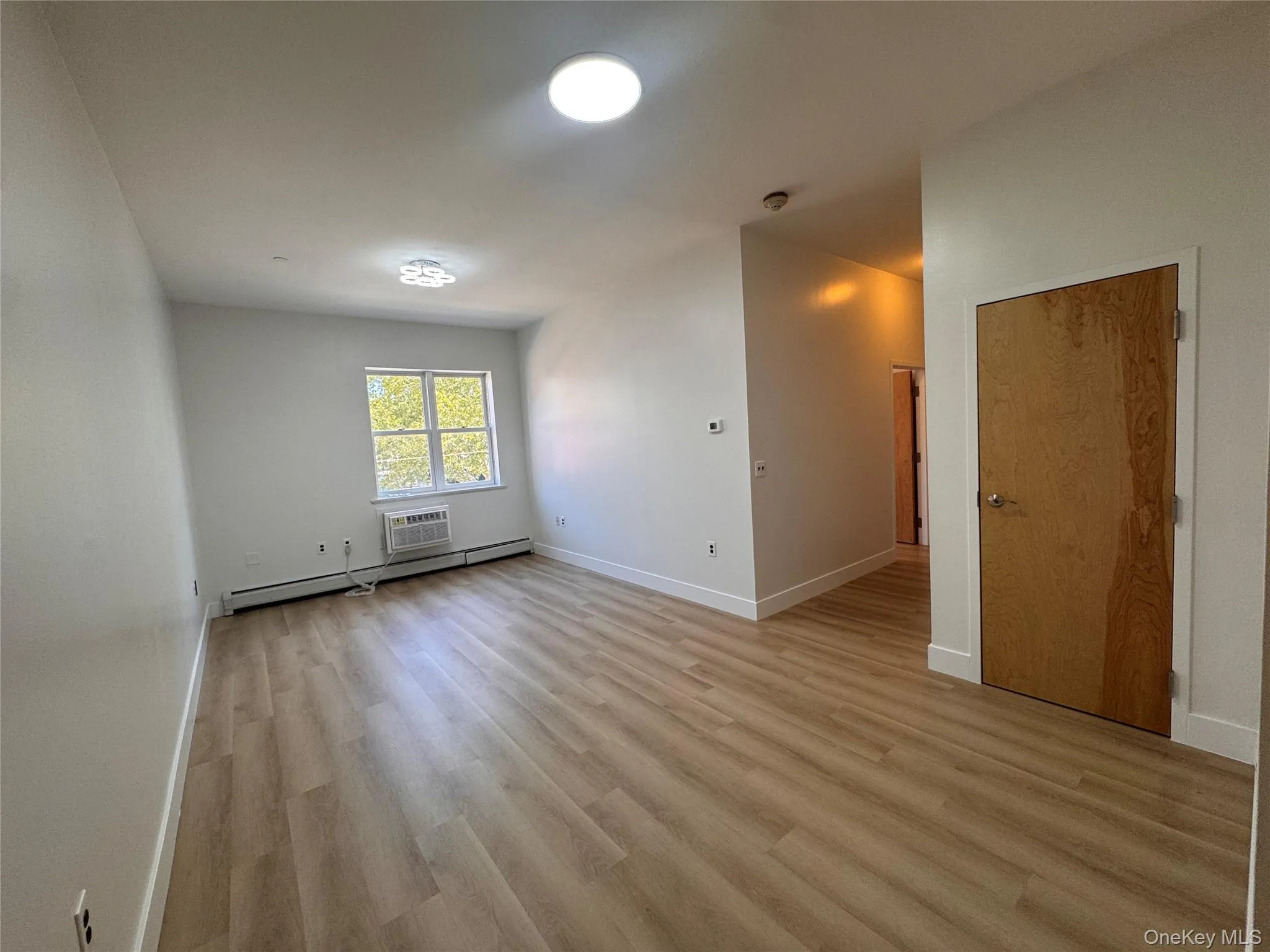 Spacious room featuring wood-finish flooring, white walls, and bright overhead lighting Spacious room featuring wood-finish flooring, white walls, and bright overhead lighting