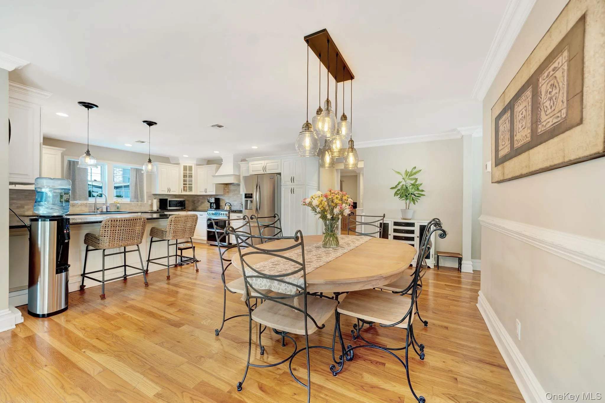 Hardwood flooring, crown molding, a built-in kitchen island with pendant lighting, white cabinetry, and stainless steel appliances Hardwood flooring, crown molding, a built-in kitchen island with pendant lighting, white cabinetry, and stainless steel appliances