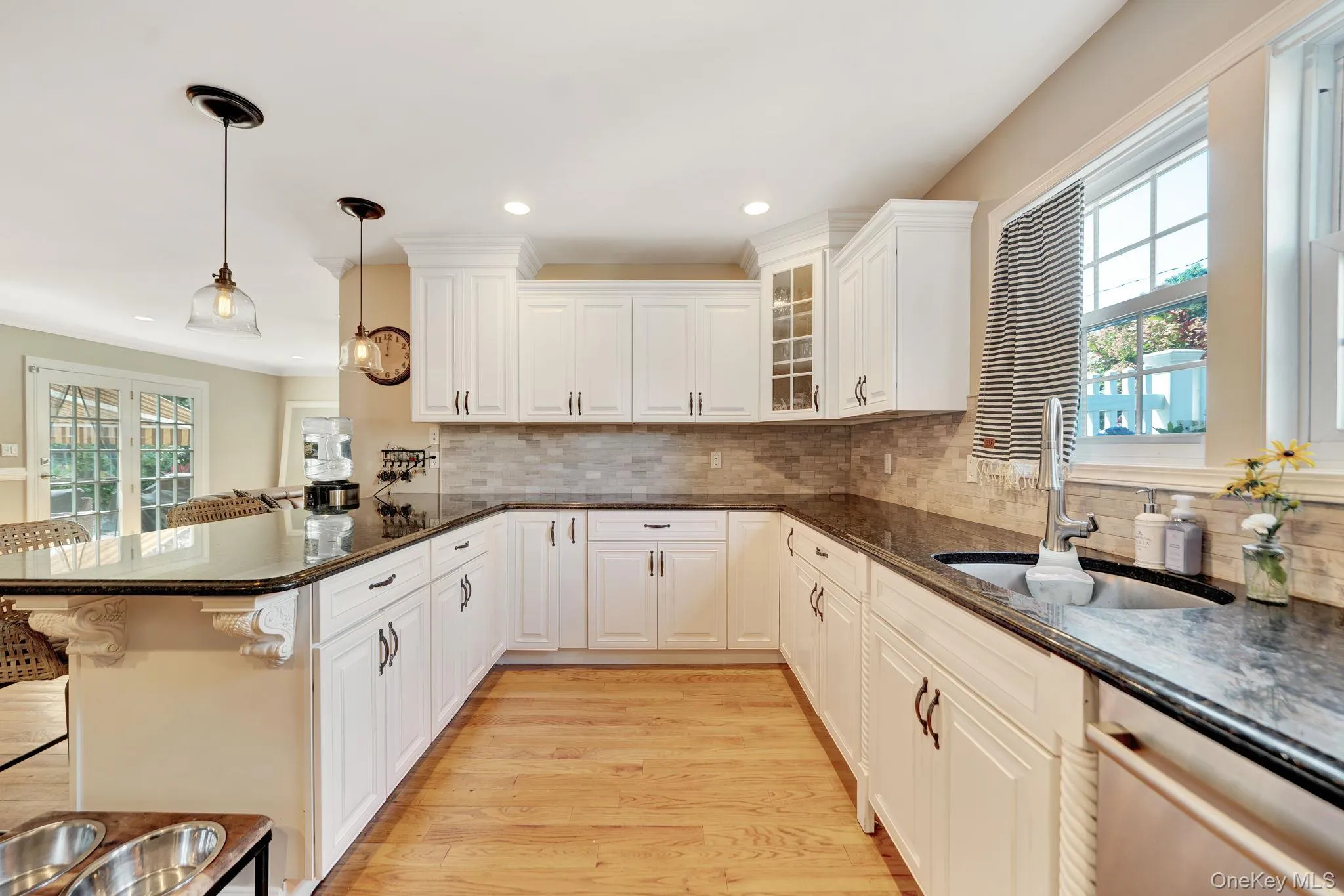U-shaped kitchen with white cabinetry, dark countertops, tile backsplash, and light wood-finish flooring U-shaped kitchen with white cabinetry, dark countertops, tile backsplash, and light wood-finish flooring