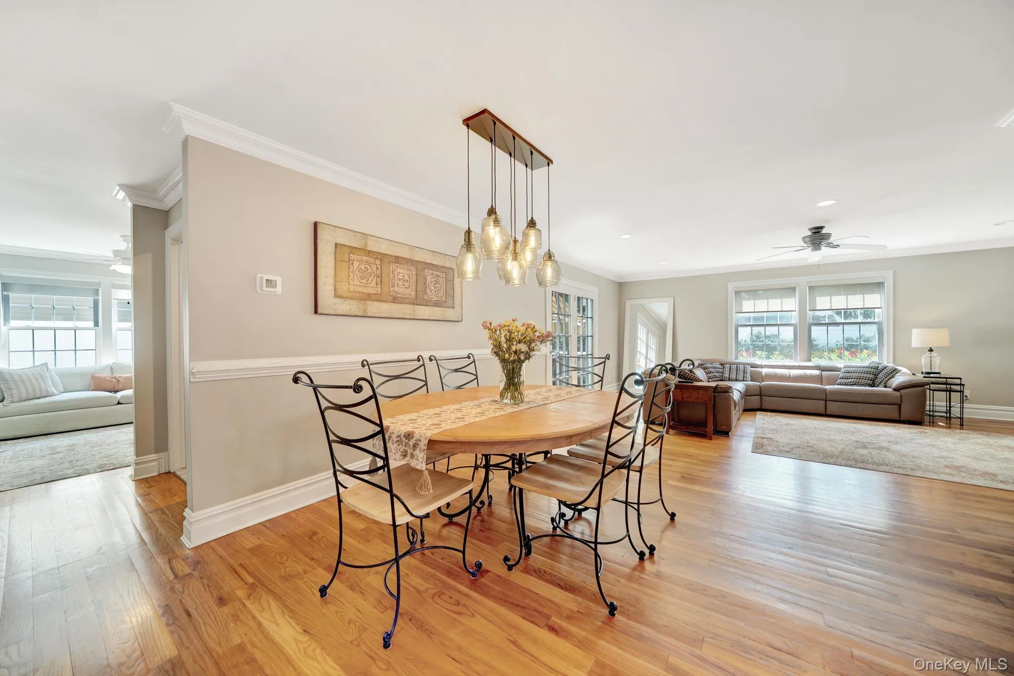 Hardwood flooring throughout, crown molding, modern multi-pendant lighting fixture, ceiling fan, and large windows Hardwood flooring throughout, crown molding, modern multi-pendant lighting fixture, ceiling fan, and large windows