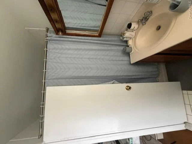 Bathroom featuring classic white subway tile, pedestal sink with chrome fixtures, wood-framed mirror, and gray patterned shower curtain Bathroom featuring classic white subway tile, pedestal sink with chrome fixtures, wood-framed mirror, and gray patterned shower curtain