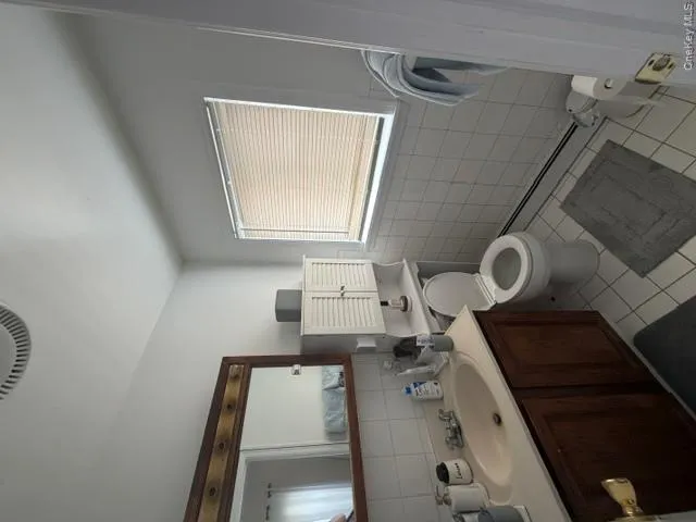 Bright bathroom featuring a dark wood vanity with an integrated sink, ceramic tile flooring in neutral tones, white subway tile walls, and a large window with blinds providing natural light Bright bathroom featuring a dark wood vanity with an integrated sink, ceramic tile flooring in neutral tones, white subway tile walls, and a large window with blinds providing natural light