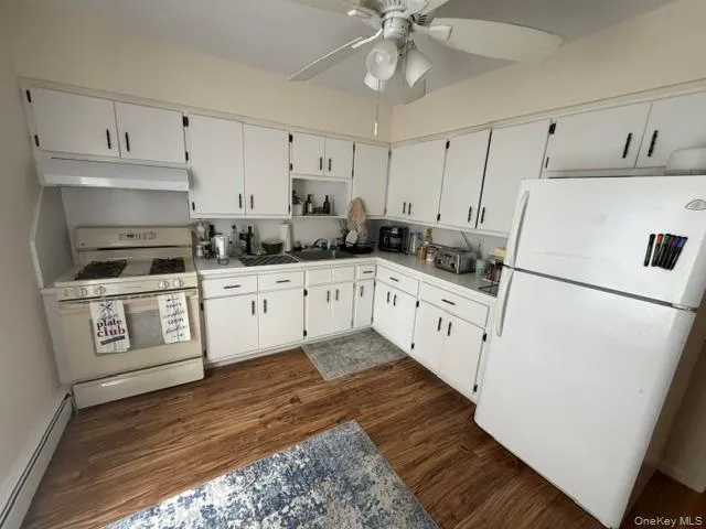 Kitchen featuring wood-finish flooring, white cabinetry with black hardware, white countertops, and a ceiling fan with integrated lighting Kitchen featuring wood-finish flooring, white cabinetry with black hardware, white countertops, and a ceiling fan with integrated lighting