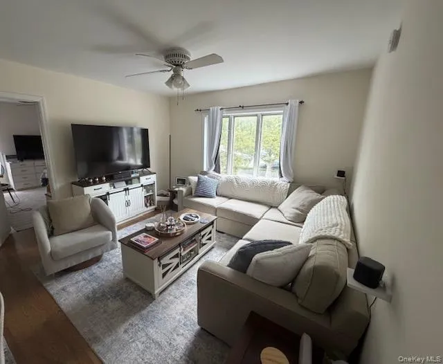 Bright, open living room featuring neutral wall finishes, ceiling fan with integrated lighting, large windows with natural light, and wood-finish flooring throughout Bright, open living room featuring neutral wall finishes, ceiling fan with integrated lighting, large windows with natural light, and wood-finish flooring throughout