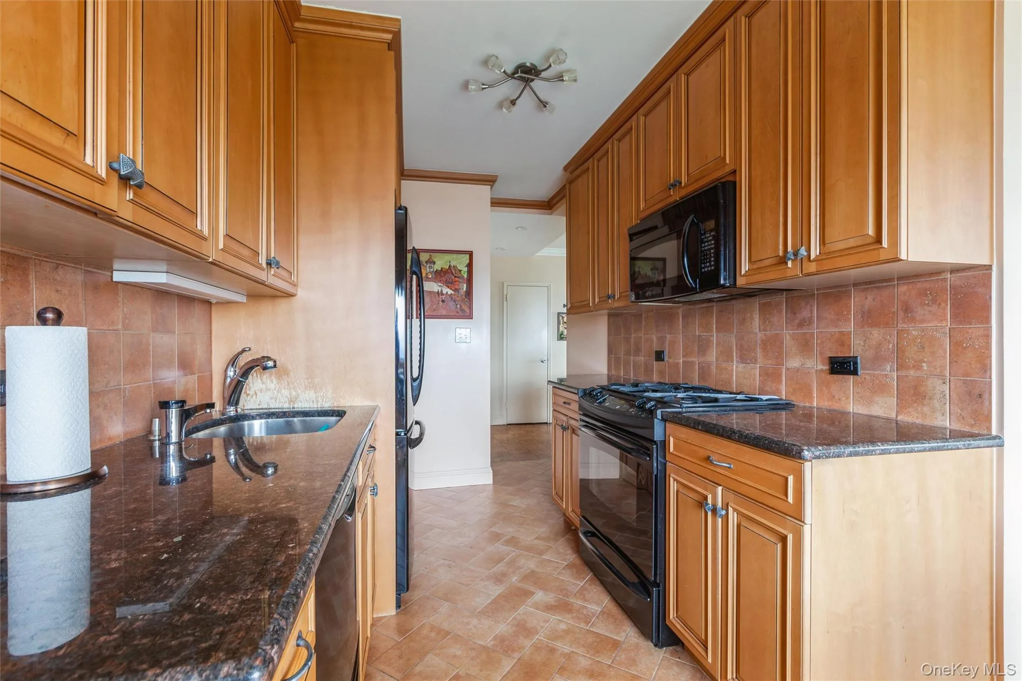 Kitchen featuring granite countertops, wood cabinetry, tile flooring, a tile backsplash, gas stove/oven, built in microwave, dishwasher. Kitchen featuring granite countertops, wood cabinetry, tile flooring, a tile backsplash, gas stove/oven, built in microwave, dishwasher.