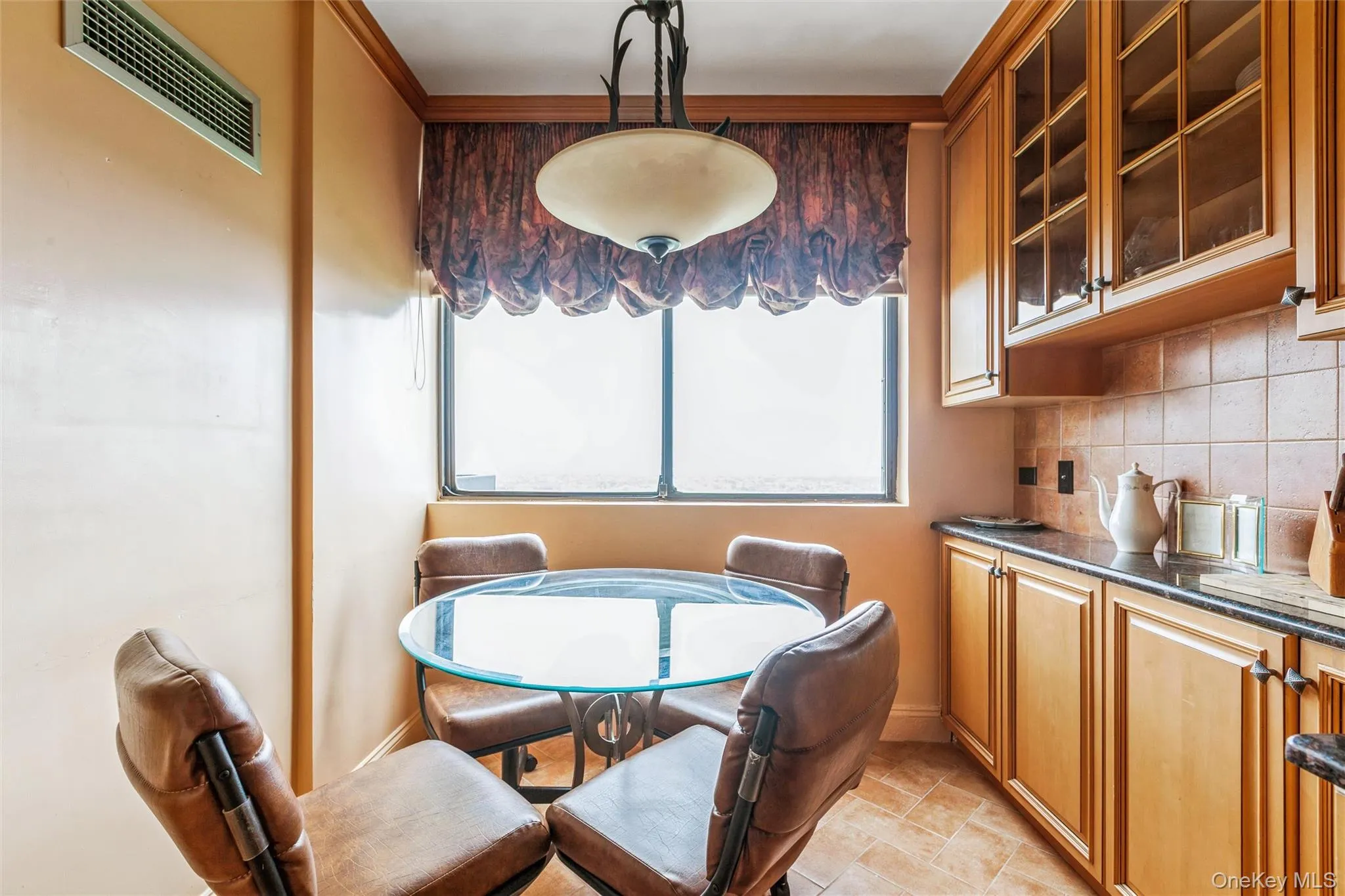 Built-in cabinetry with glass-front upper cabinets, tile backsplash, dark countertops, tile flooring and tons of natural light. Built-in cabinetry with glass-front upper cabinets, tile backsplash, dark countertops, tile flooring and tons of natural light.