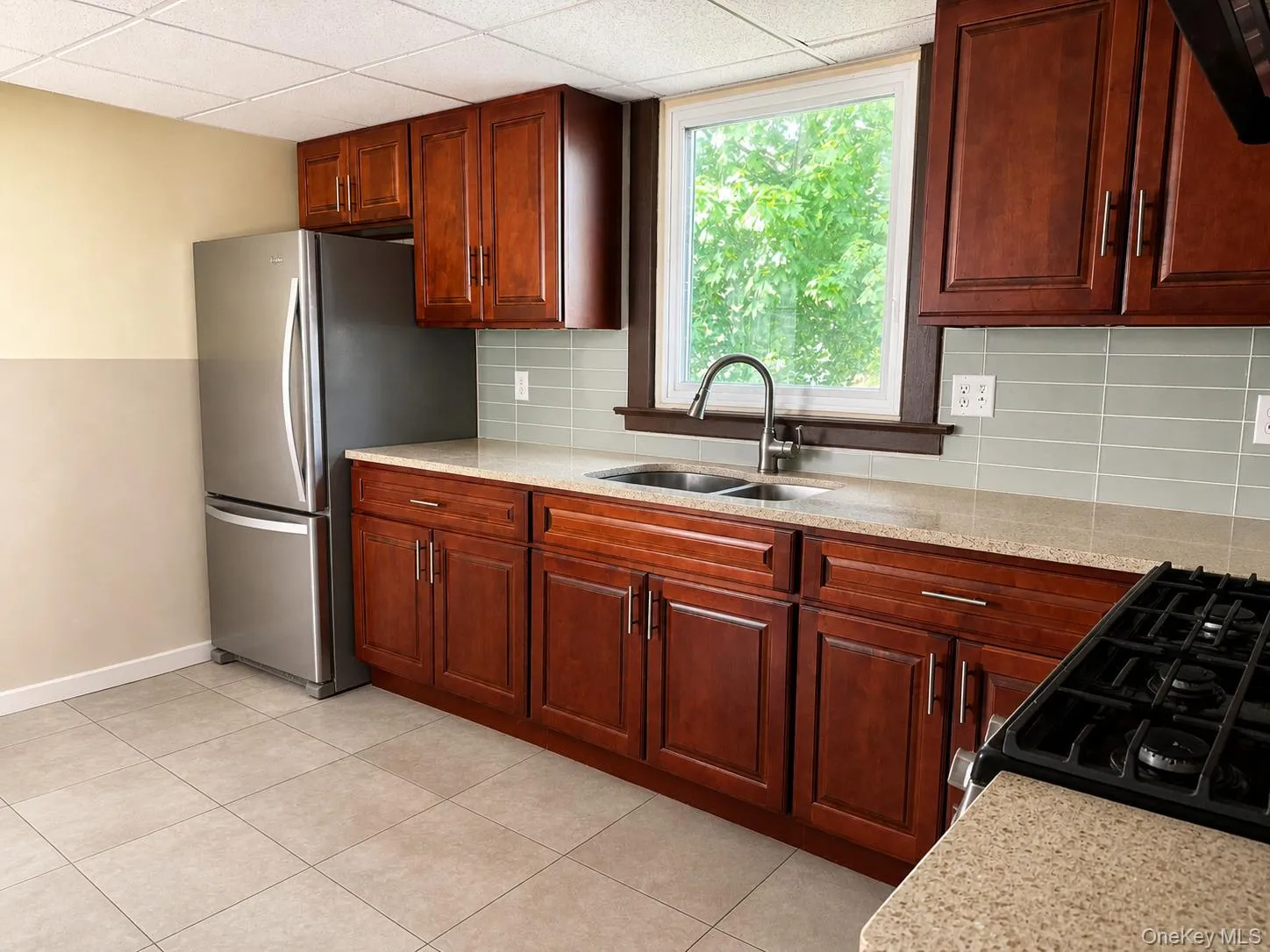 Kitchen featuring rich wood cabinetry, light-toned countertops, a stainless steel refrigerator, and a tile backsplash Kitchen featuring rich wood cabinetry, light-toned countertops, a stainless steel refrigerator, and a tile backsplash