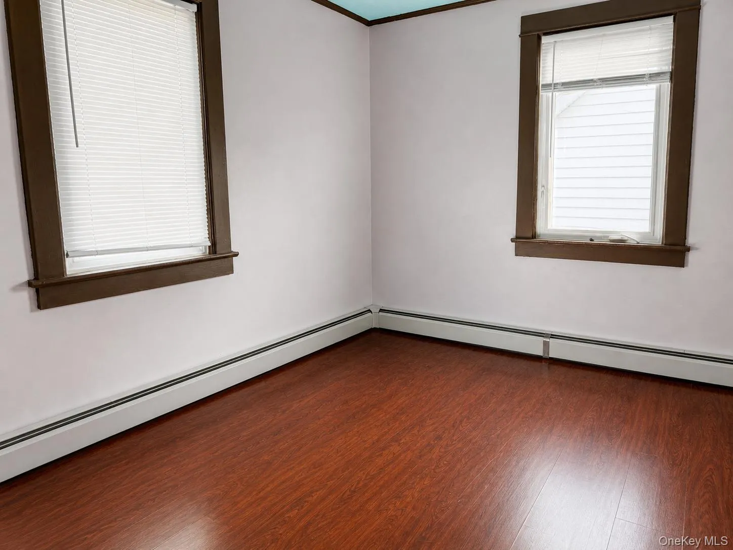 Wood-finish flooring complemented by white walls and two windows with brown trim Wood-finish flooring complemented by white walls and two windows with brown trim