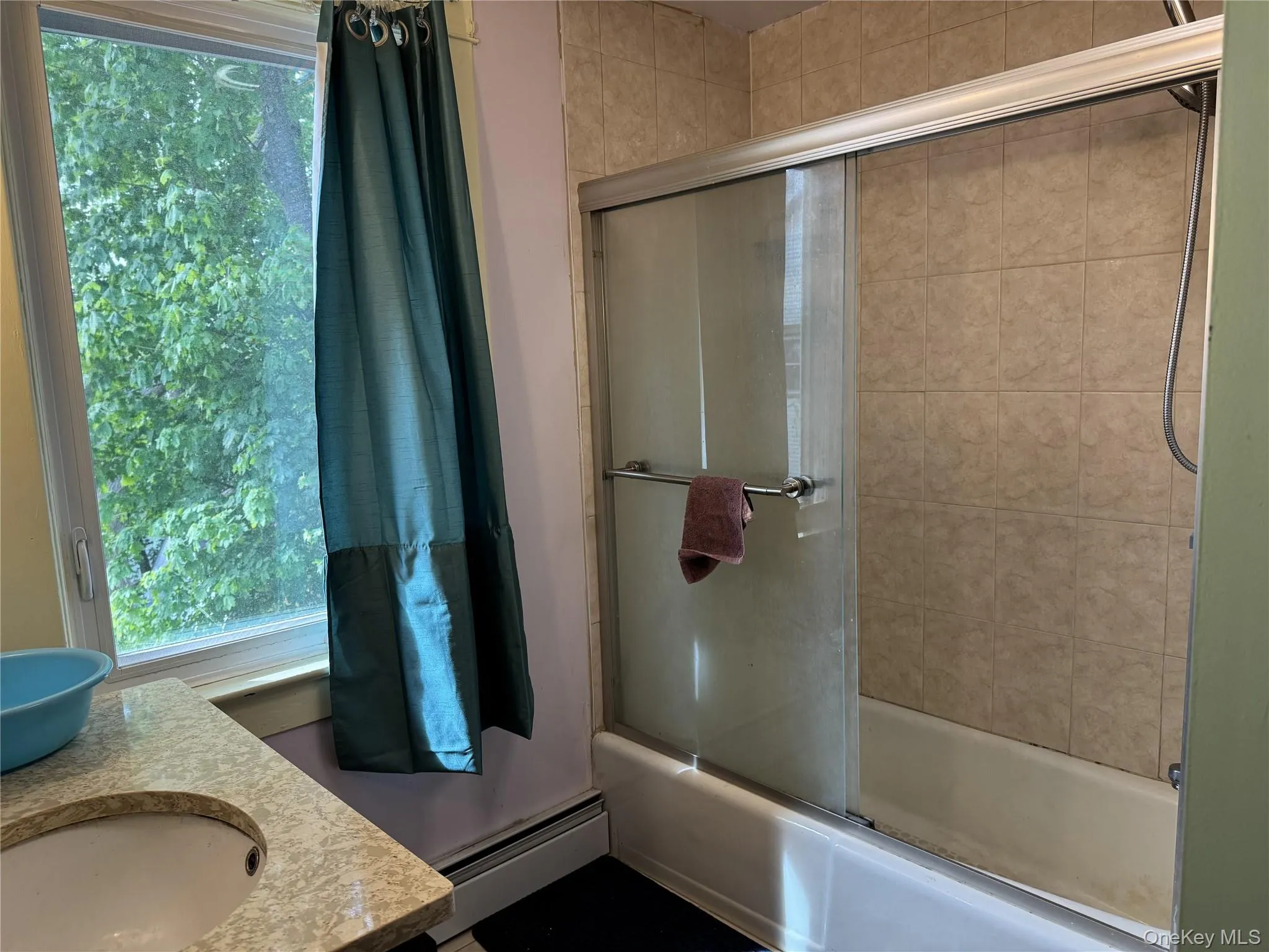 Bathtub with sliding glass enclosure, tiled shower surround, integrated vanity sink, and window Bathtub with sliding glass enclosure, tiled shower surround, integrated vanity sink, and window