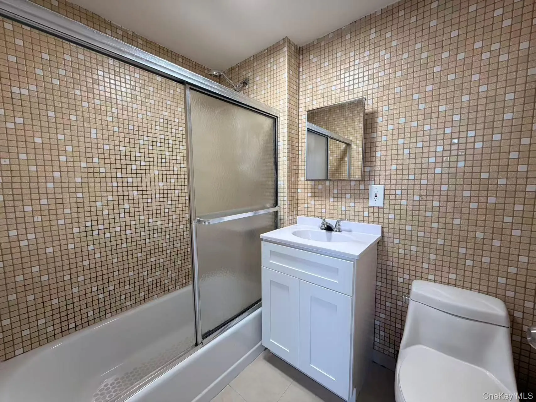 Full bathroom with tile walls, shower / bath combination with glass door, light tile patterned floors, and vanity Full bathroom with tile walls, shower / bath combination with glass door, light tile patterned floors, and vanity