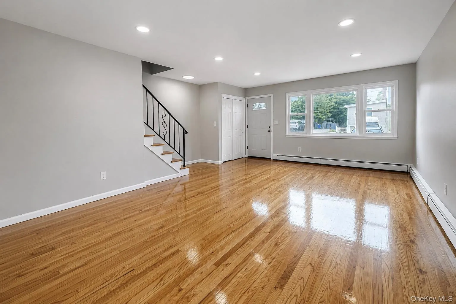 Hardwood flooring, recessed ceiling lighting, a staircase with a black metal railing, two-panel sliding closet doors, and a window Hardwood flooring, recessed ceiling lighting, a staircase with a black metal railing, two-panel sliding closet doors, and a window