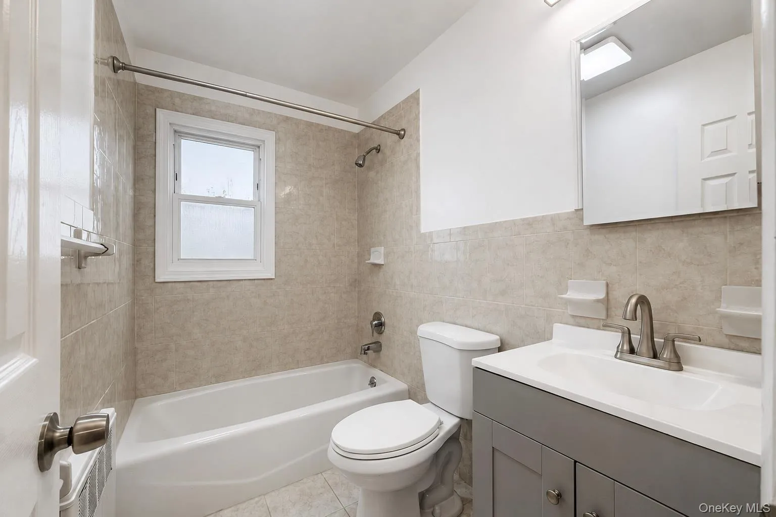 Full bathroom featuring a white bathtub, tiled walls, a window, a white vanity with a single sink, and a mounted mirror Full bathroom featuring a white bathtub, tiled walls, a window, a white vanity with a single sink, and a mounted mirror