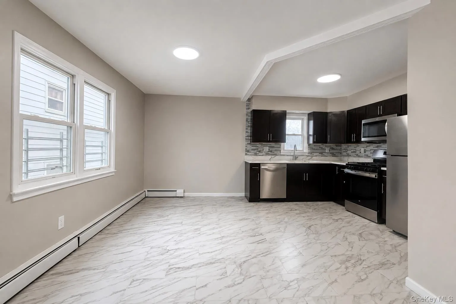 Open-concept kitchen and living area featuring dark wood-finish cabinetry, stainless steel appliances, and a mosaic tile backsplash Open-concept kitchen and living area featuring dark wood-finish cabinetry, stainless steel appliances, and a mosaic tile backsplash