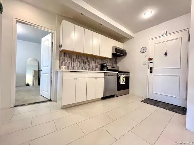Kitchen with appliances with stainless steel finishes, tasteful backsplash, white cabinetry, light countertops, and arched walkways Kitchen with appliances with stainless steel finishes, tasteful backsplash, white cabinetry, light countertops, and arched walkways