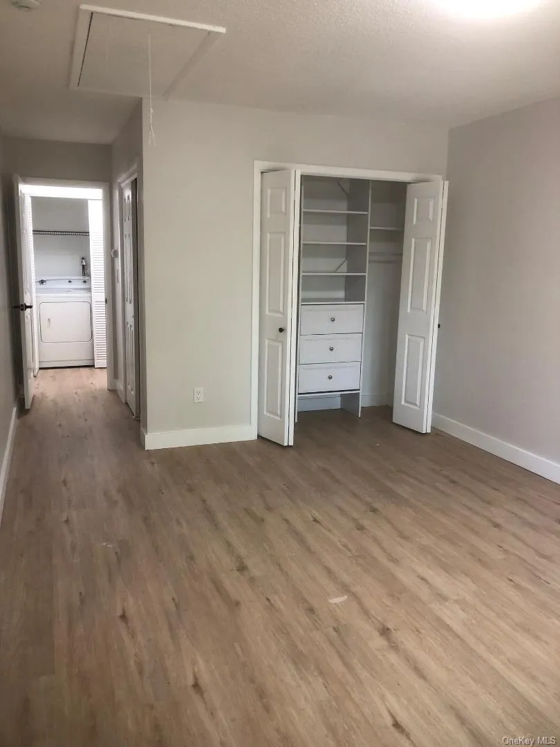 Spacious primary bedroom featuring wood-like flooring, 2 double closets - oen with built-in closet organization system with shelving and drawers, a white bi-fold closet door, and contemporary light gray wall paint Spacious primary bedroom featuring wood-like flooring, 2 double closets - oen with built-in closet organization system with shelving and drawers, a white bi-fold closet door, and contemporary light gray wall paint